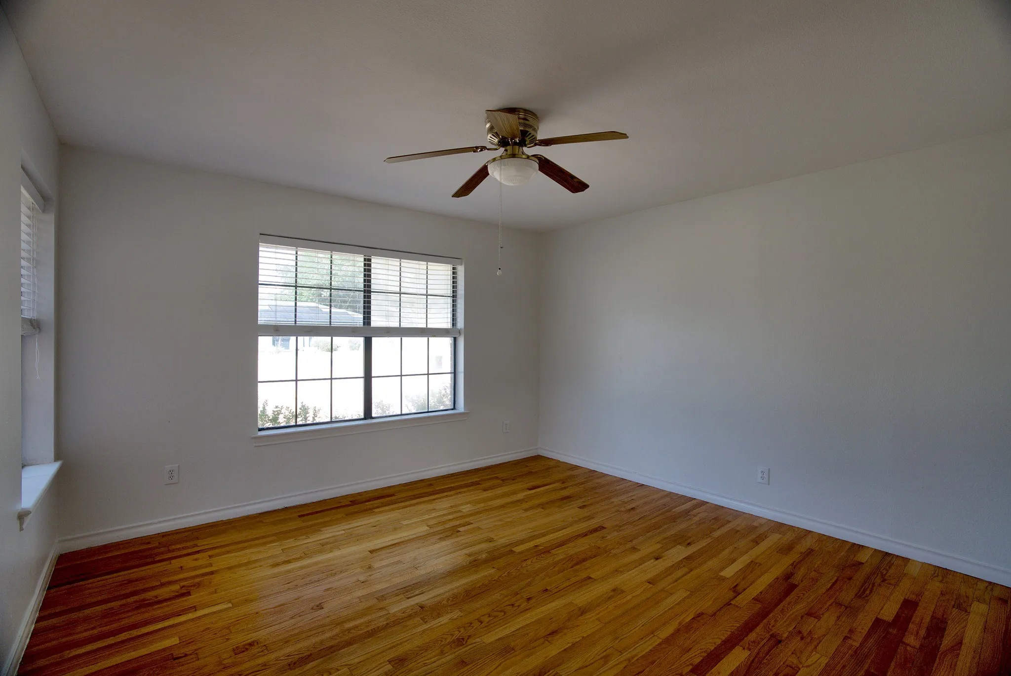 Hardwood flooring, white walls, two windows with blinds, and a ceiling fan