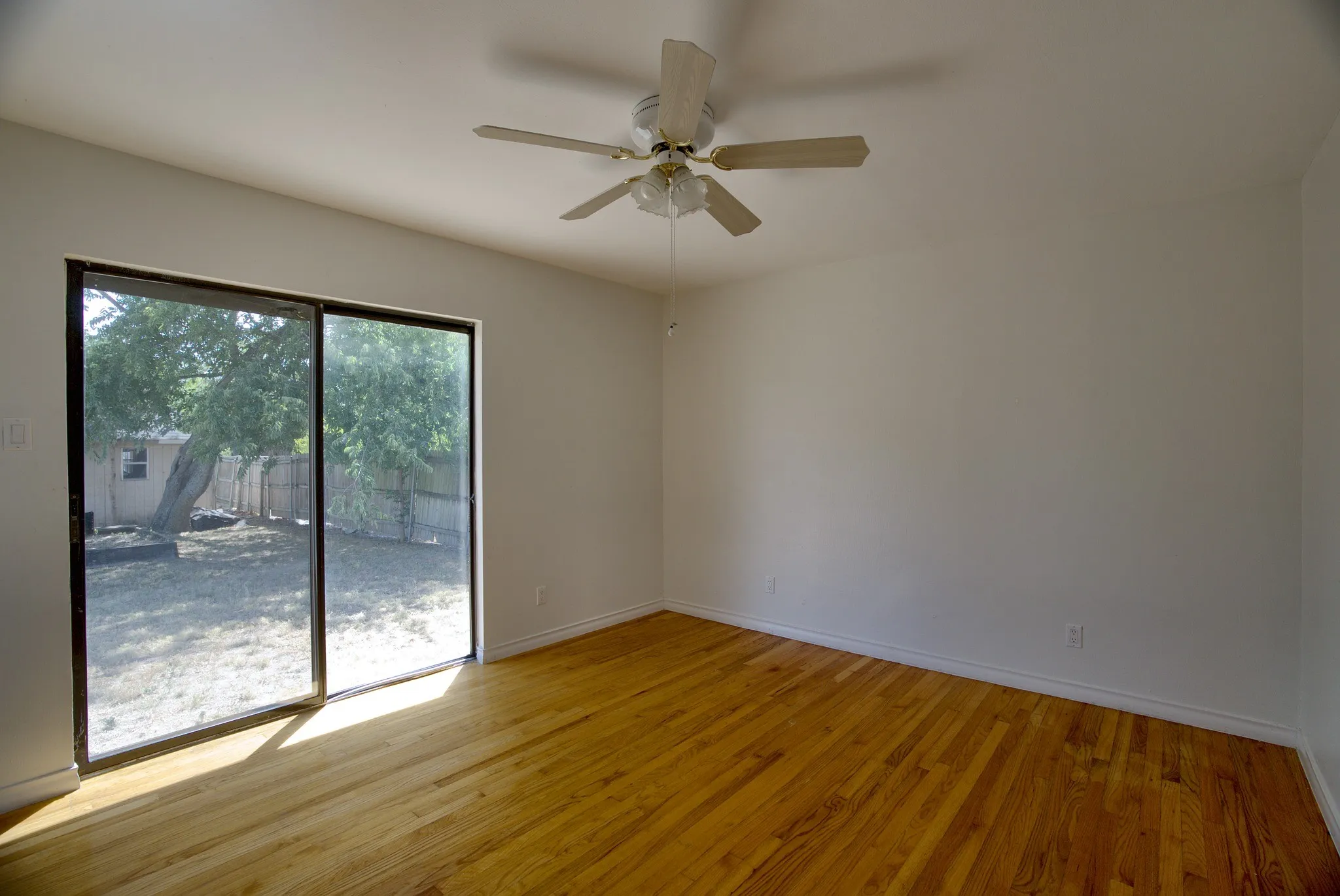 Wood-finish flooring, sliding glass door, white walls, and a ceiling fan