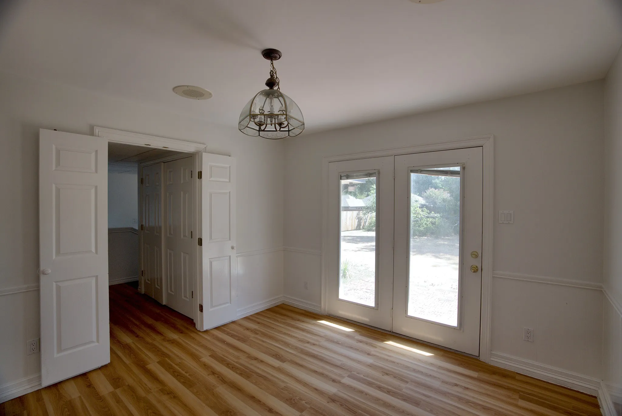 Wood-finish flooring, white paneled double doors, glass-paneled patio doors, decorative wainscoting, and an ornamental ceiling fixture