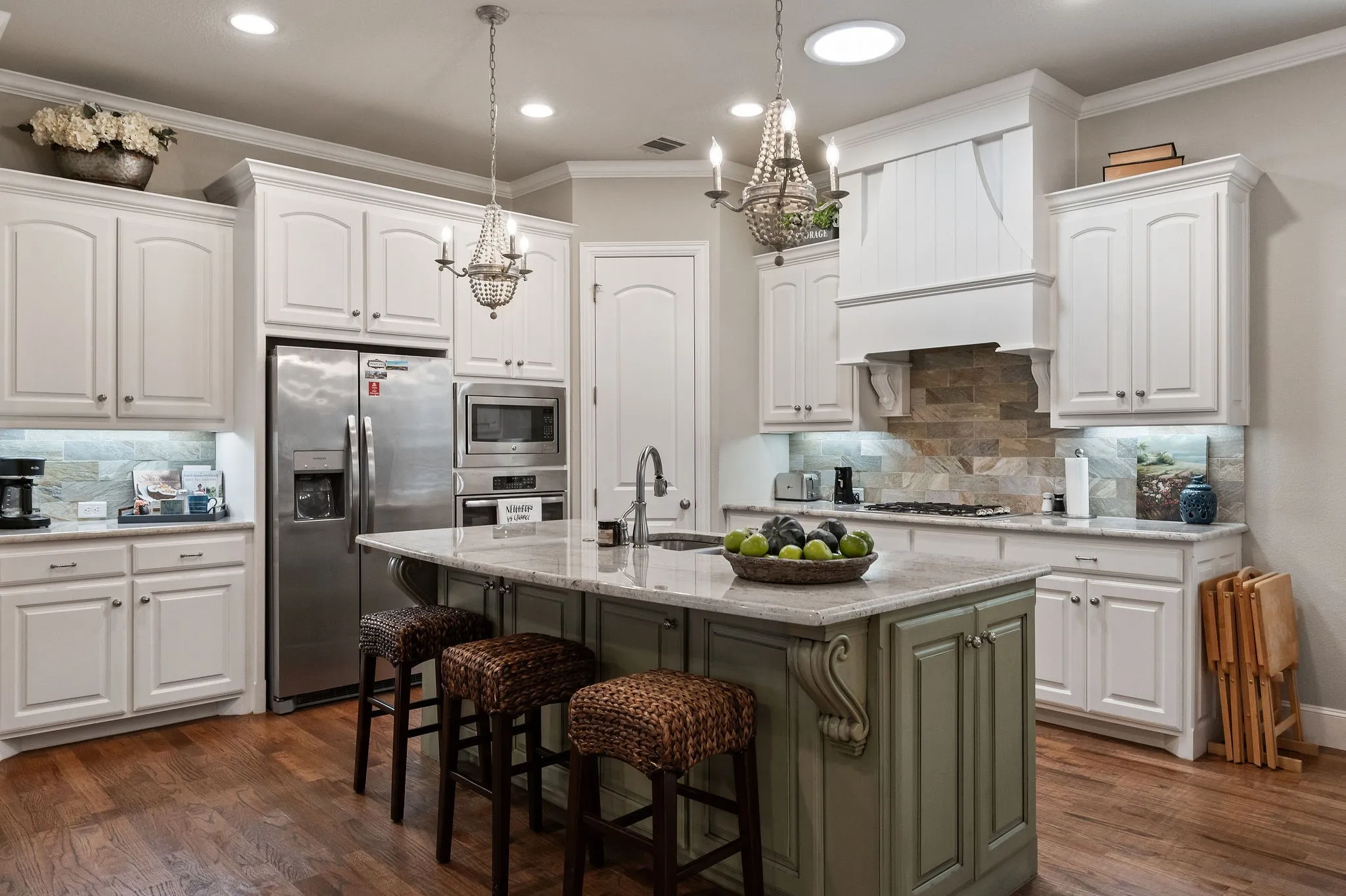 Kitchen featuring a central island with counter seating, wood-finish flooring, white cabinetry, integrated stainless steel appliances, and a tiled backsplash