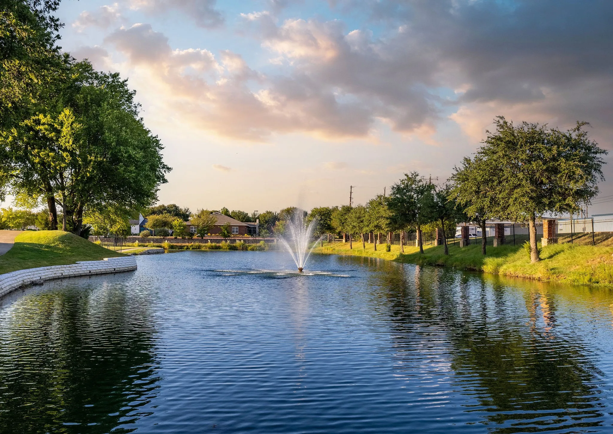 Water feature with a fountain, surrounded by manicured landscaping and mature trees