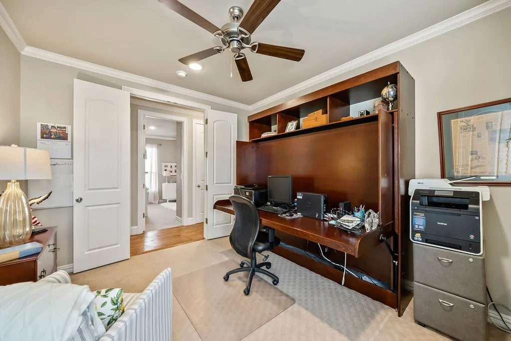 Built-in wood-finish desk with integrated shelving, ceiling fan with wood-finish blades, recessed lighting, and white crown molding