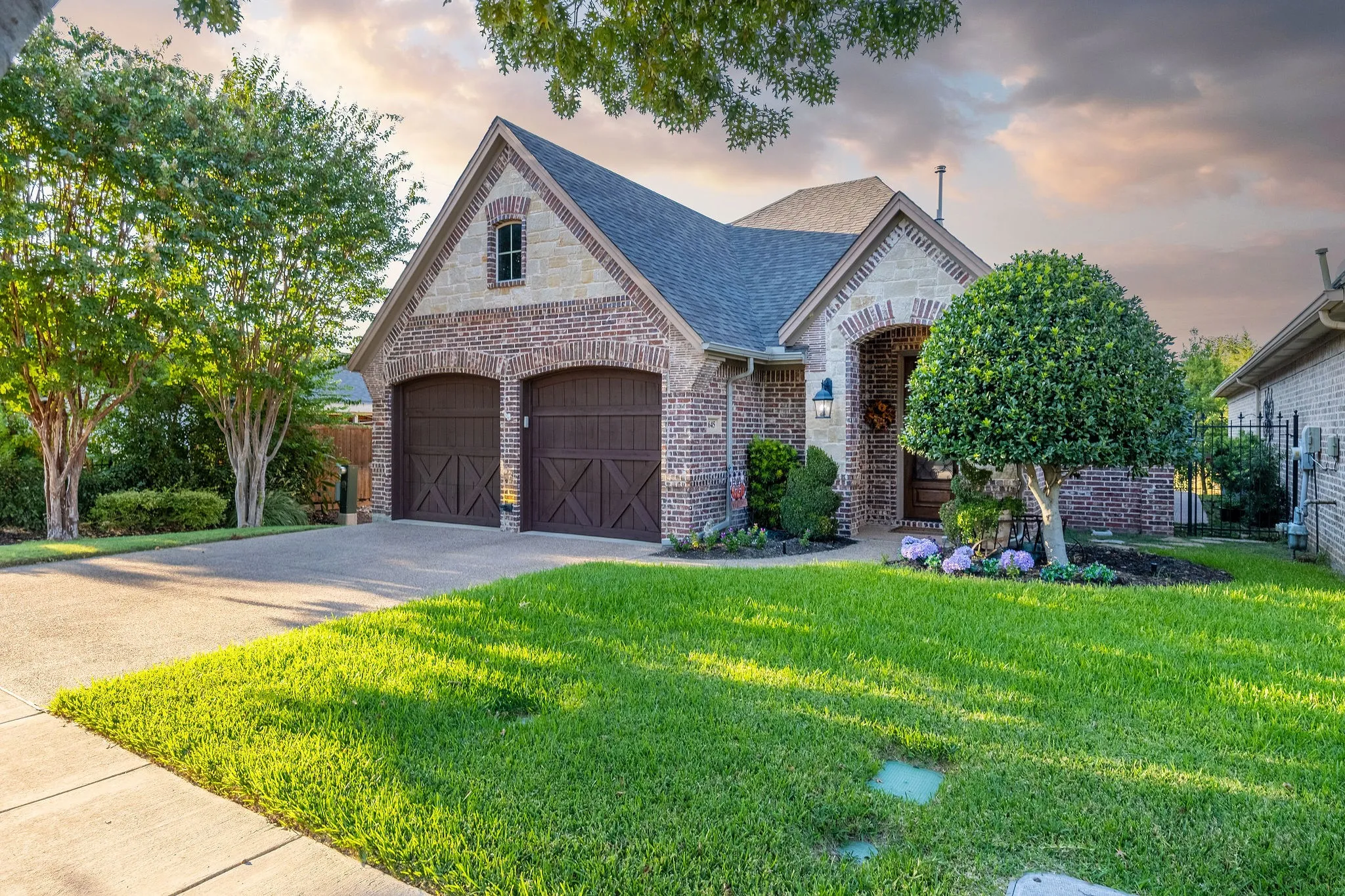 Brick and stone exterior with arched accents, pitched roof, and dual wood-finish garage doors