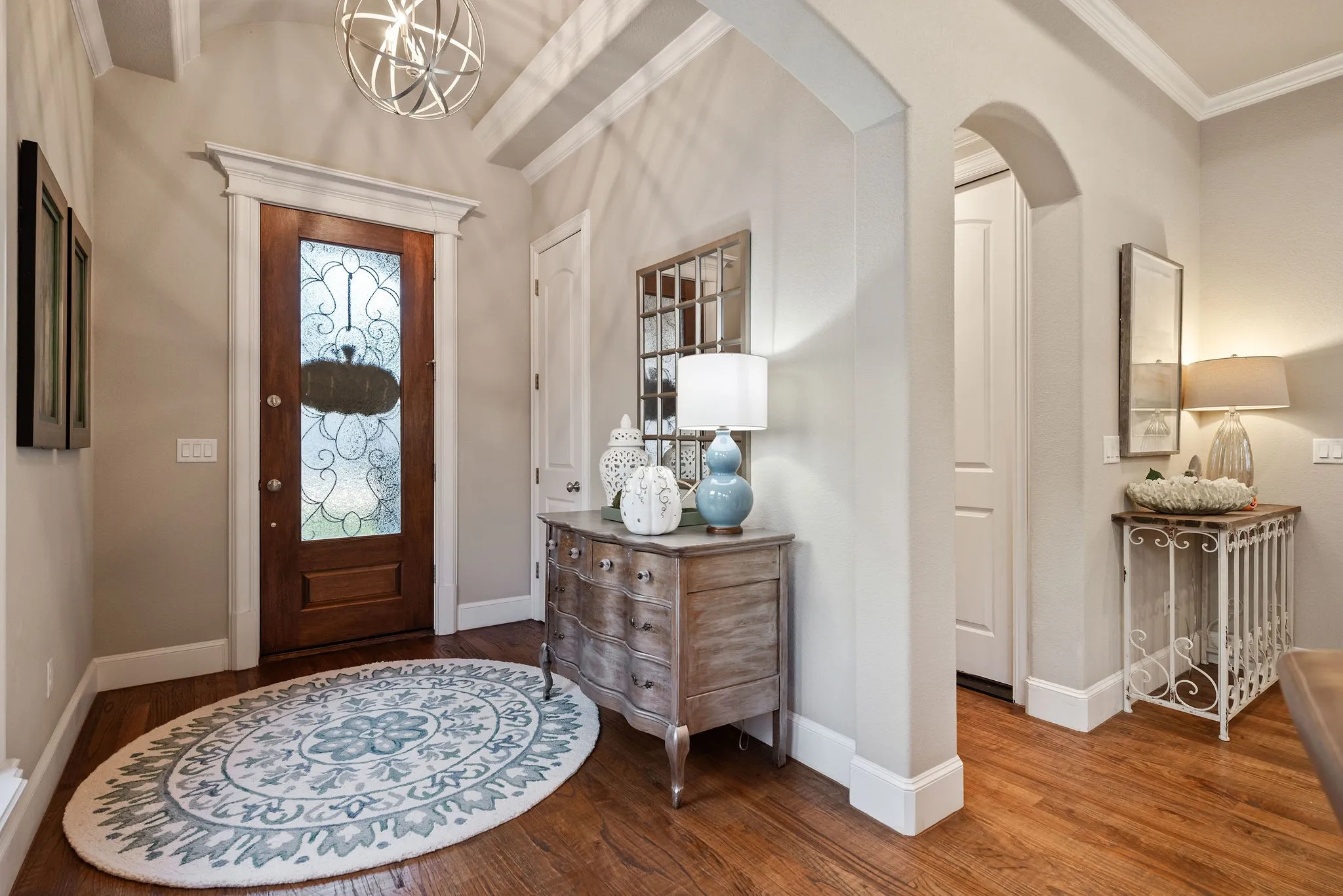 Hardwood flooring, arched doorway, decorative transom above entry, decorative entry door with patterned glass, ceiling with exposed beams