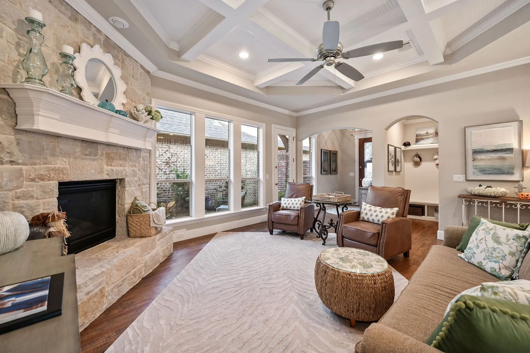 Stone fireplace with a white mantel, wood-finish flooring, coffer ceiling with recessed lighting, ceiling fan, and arched doorways