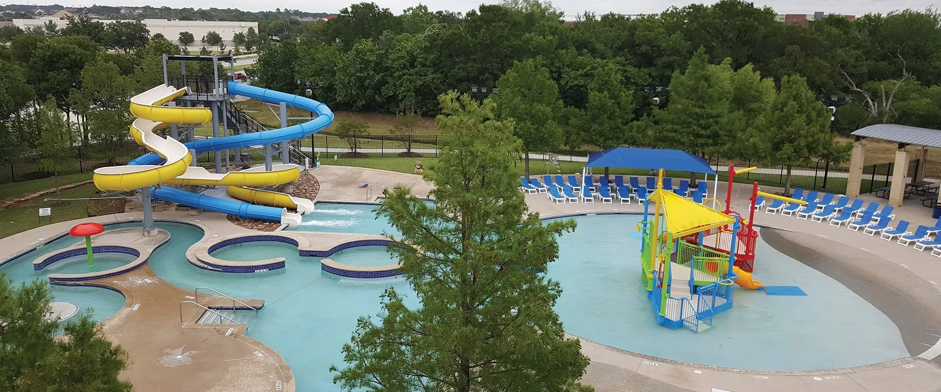 Water park area featuring multiple water slides, a wading pool with interactive play equipment, a lazy river, and a shaded seating area
