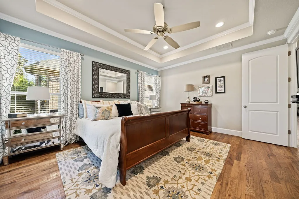 Wood-finish flooring, recessed lighting, ceiling fan, and tray ceiling with crown molding