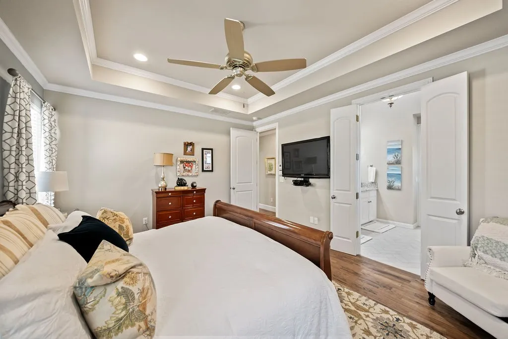 Tray ceiling with recessed lighting and crown molding, wood-finish flooring, ceiling fan, and double doors to an adjoining space