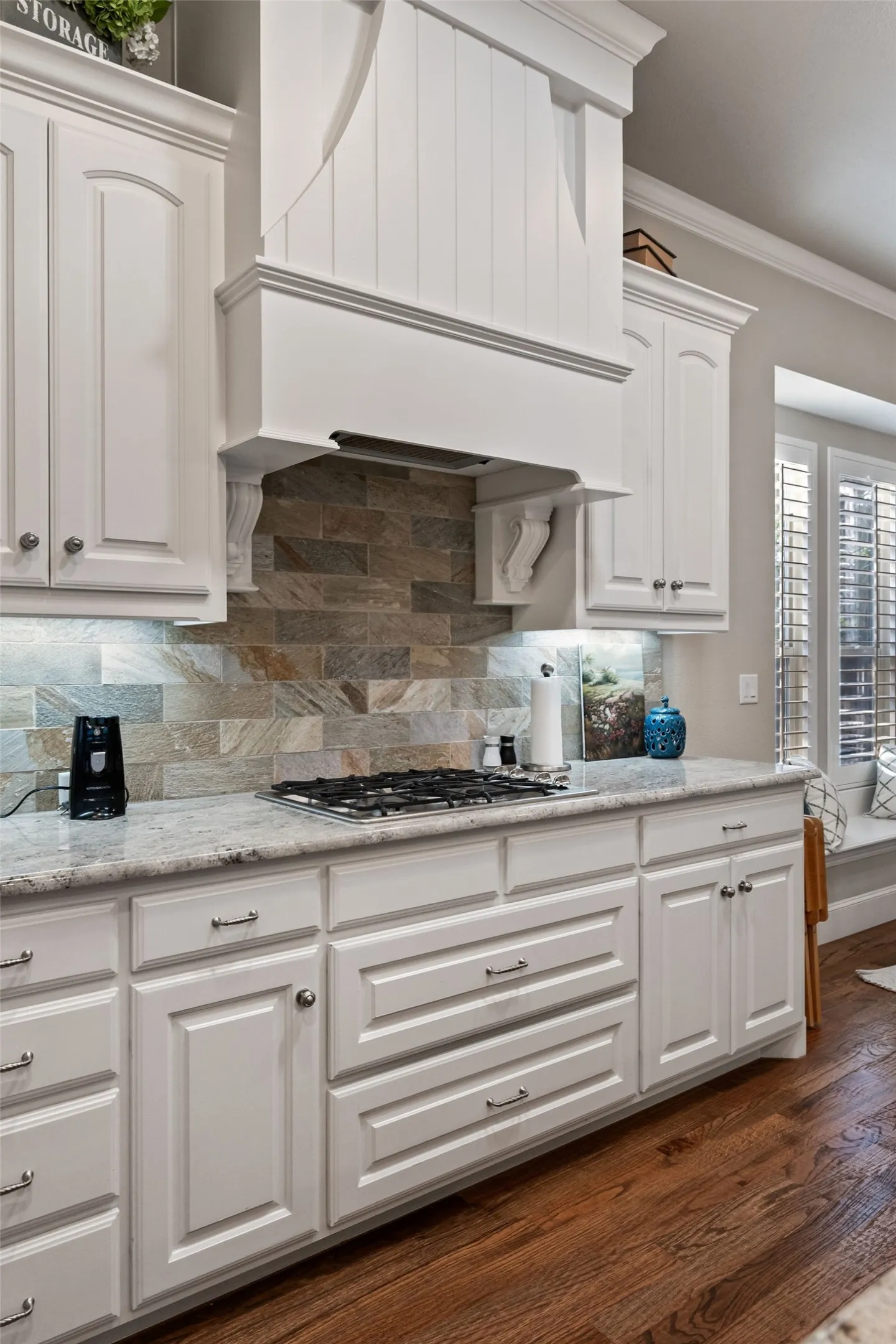 White cabinetry, gas cooktop, granite countertops, stone backsplash, and wood-finish flooring
