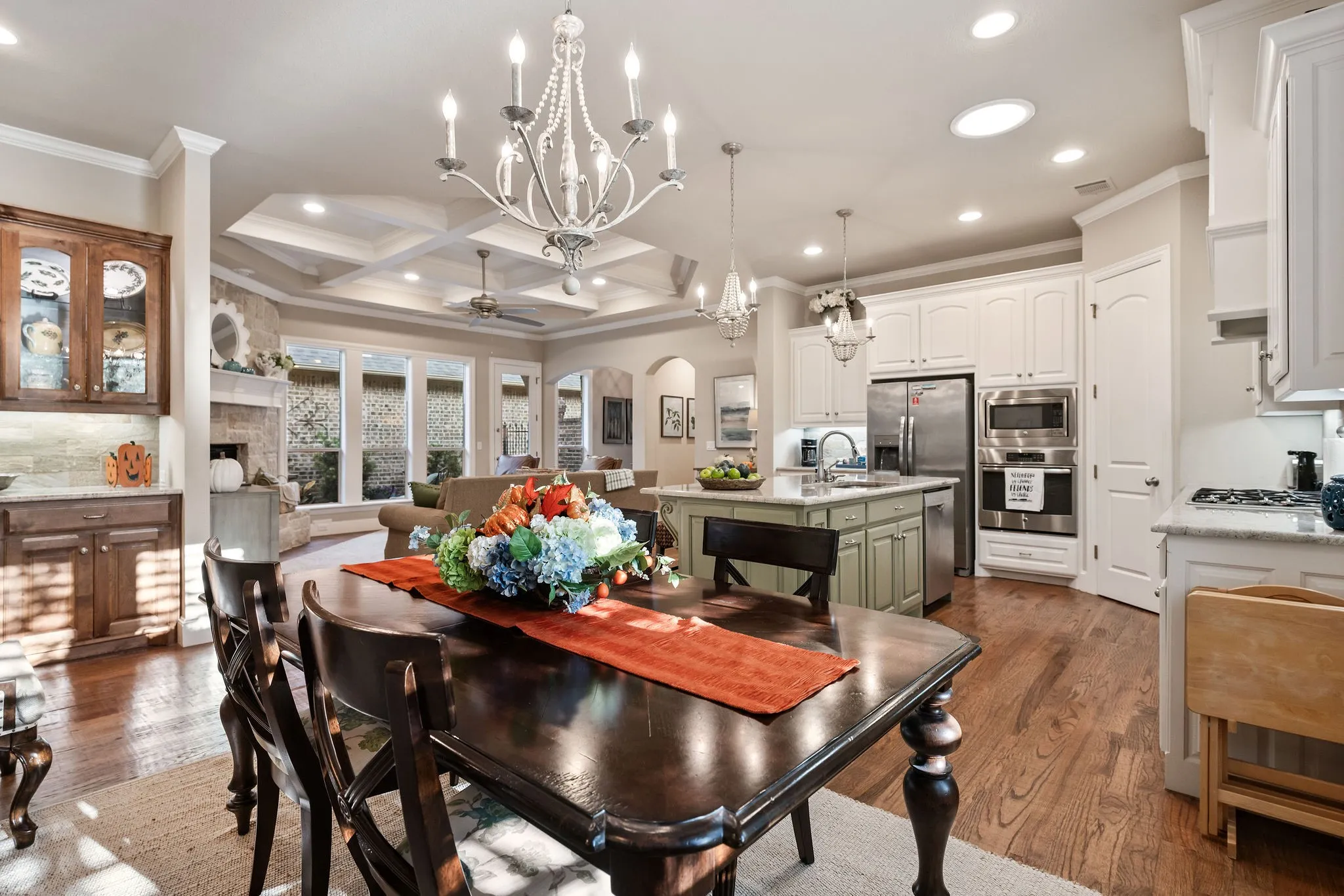 Hardwood flooring throughout, coffered ceiling in the living area, kitchen island with sink, built-in stainless steel appliances, and a stone fireplace