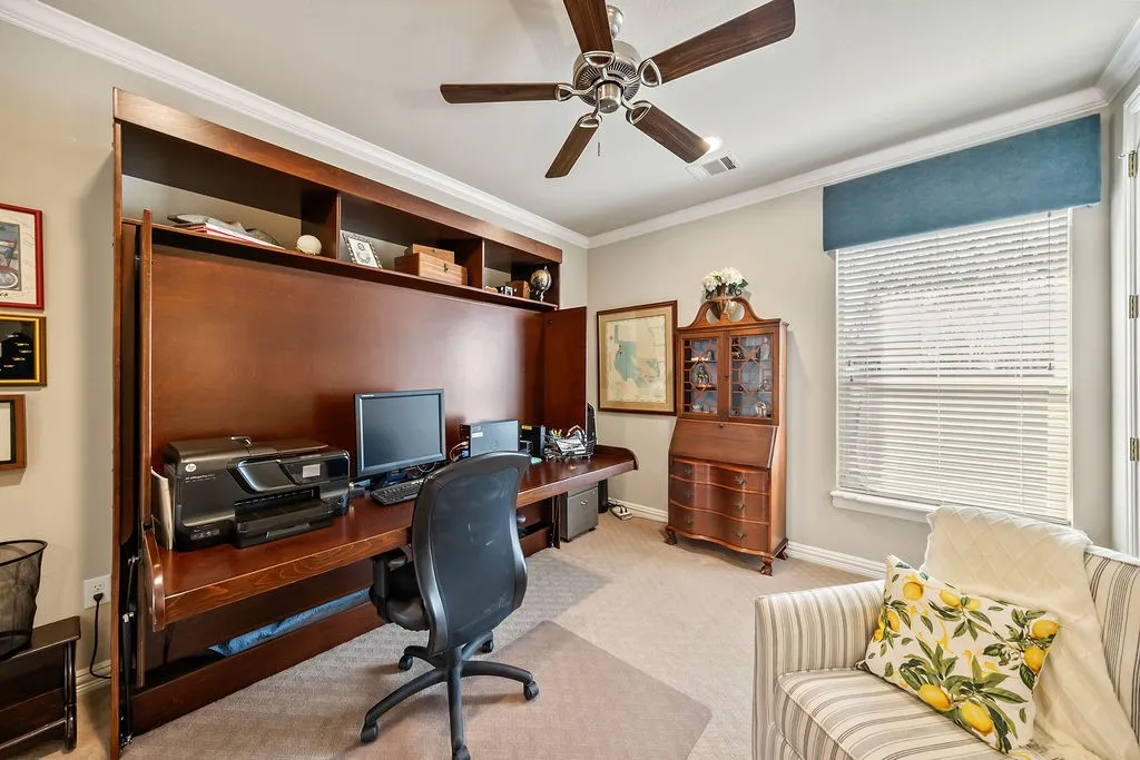Built-in wood-finish wall unit with integrated desk and shelving, ceiling fan with wood-tone blades, and a window with blinds