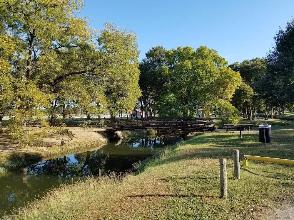 Lush green space featuring mature trees, a tranquil waterway, and a pedestrian bridge