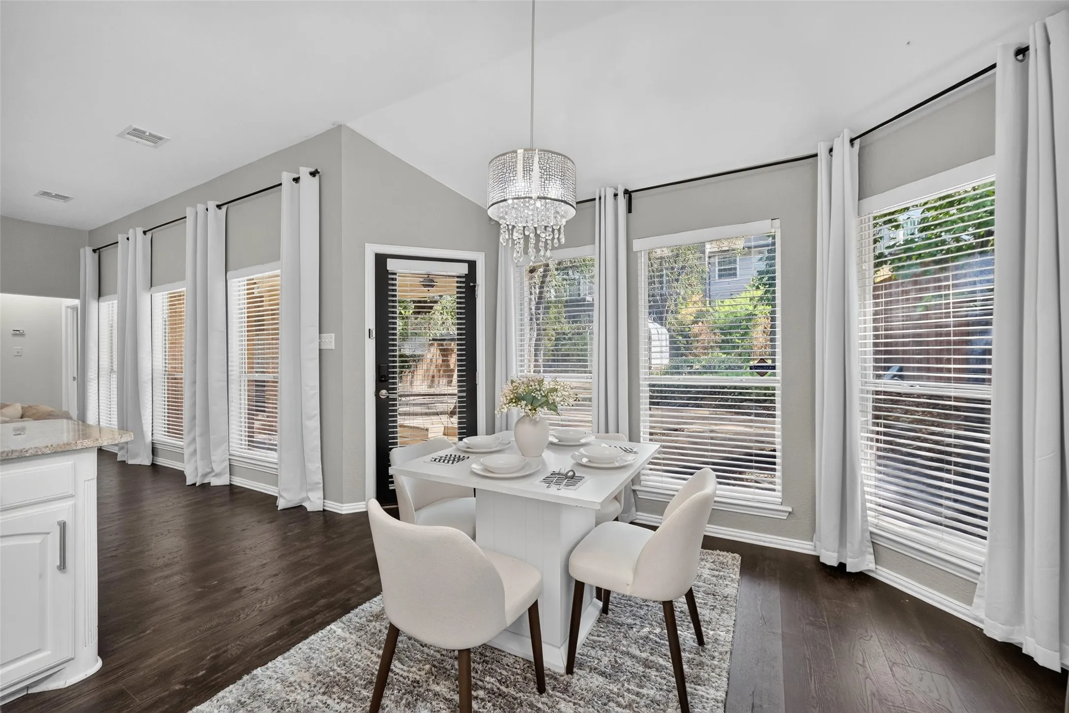 Dark wood-finish flooring, vaulted ceiling, and multiple windows with blinds