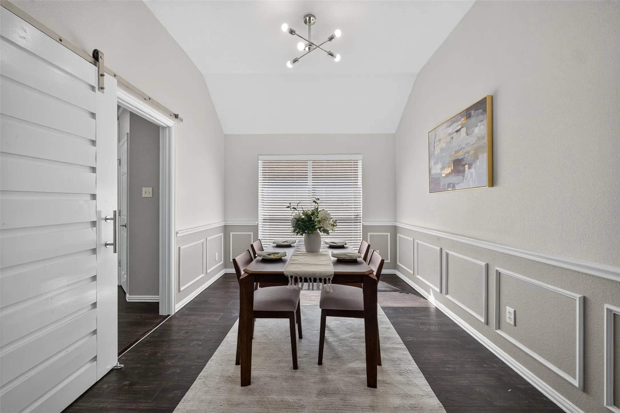 Vaulted ceiling with an updated lighting fixture, wood-finish flooring, half-wall wainscoting, and a window with horizontal blinds