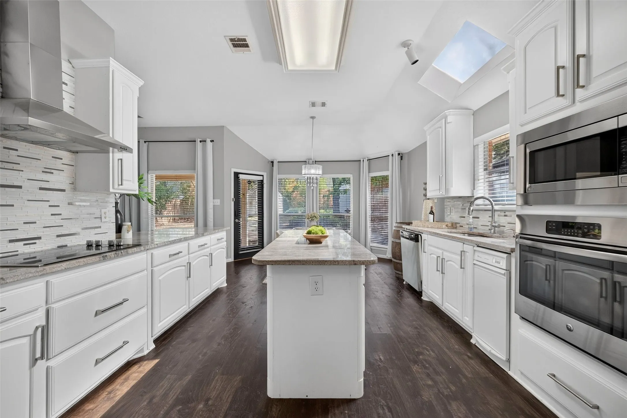 Kitchen featuring white cabinetry, stainless steel appliances, a center island with countertop, hardwood-finish flooring, and a skylight