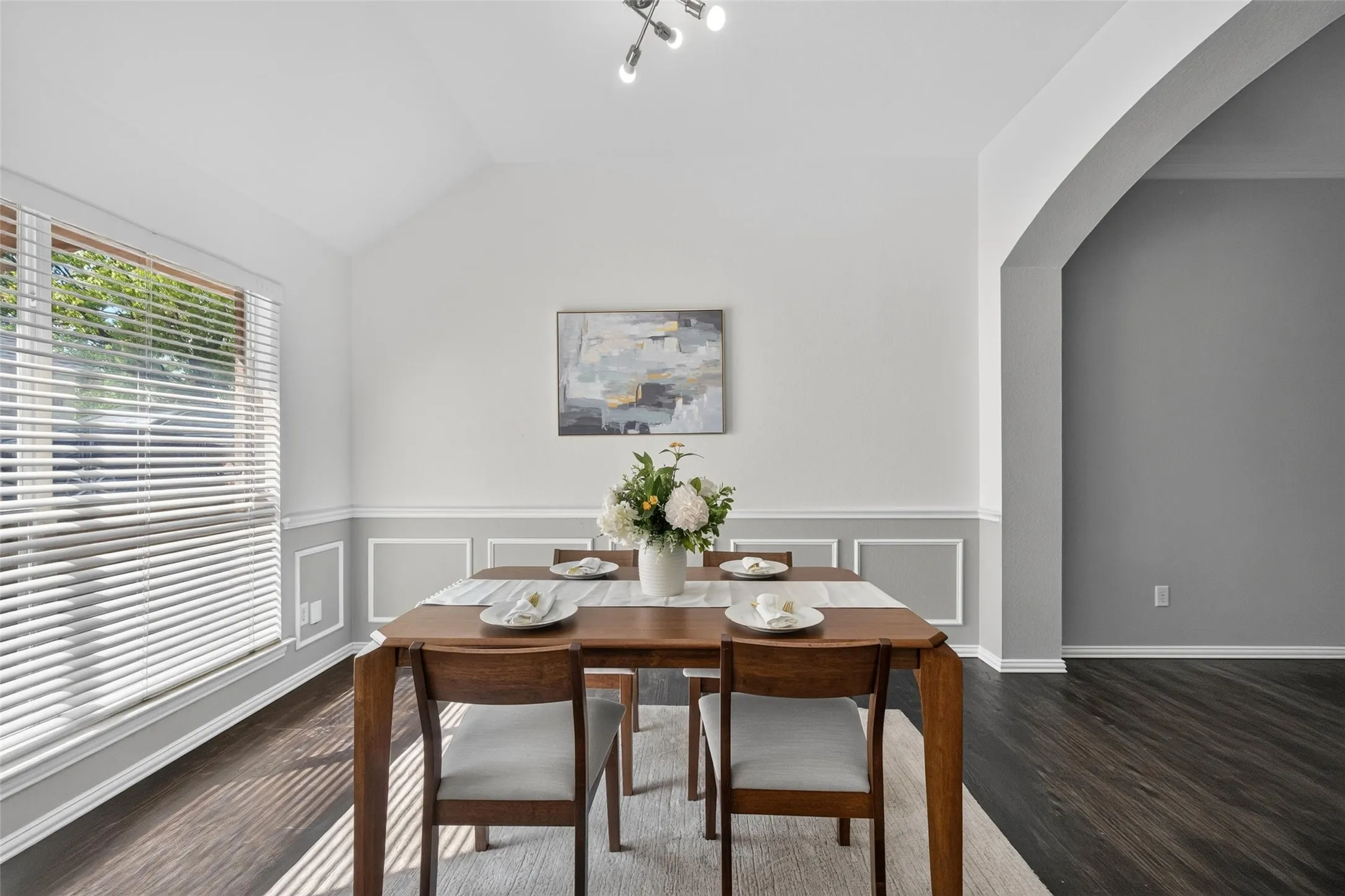 Vaulted ceiling, recessed lighting, wood-finish flooring, accent wall paneling, and an arched entryway