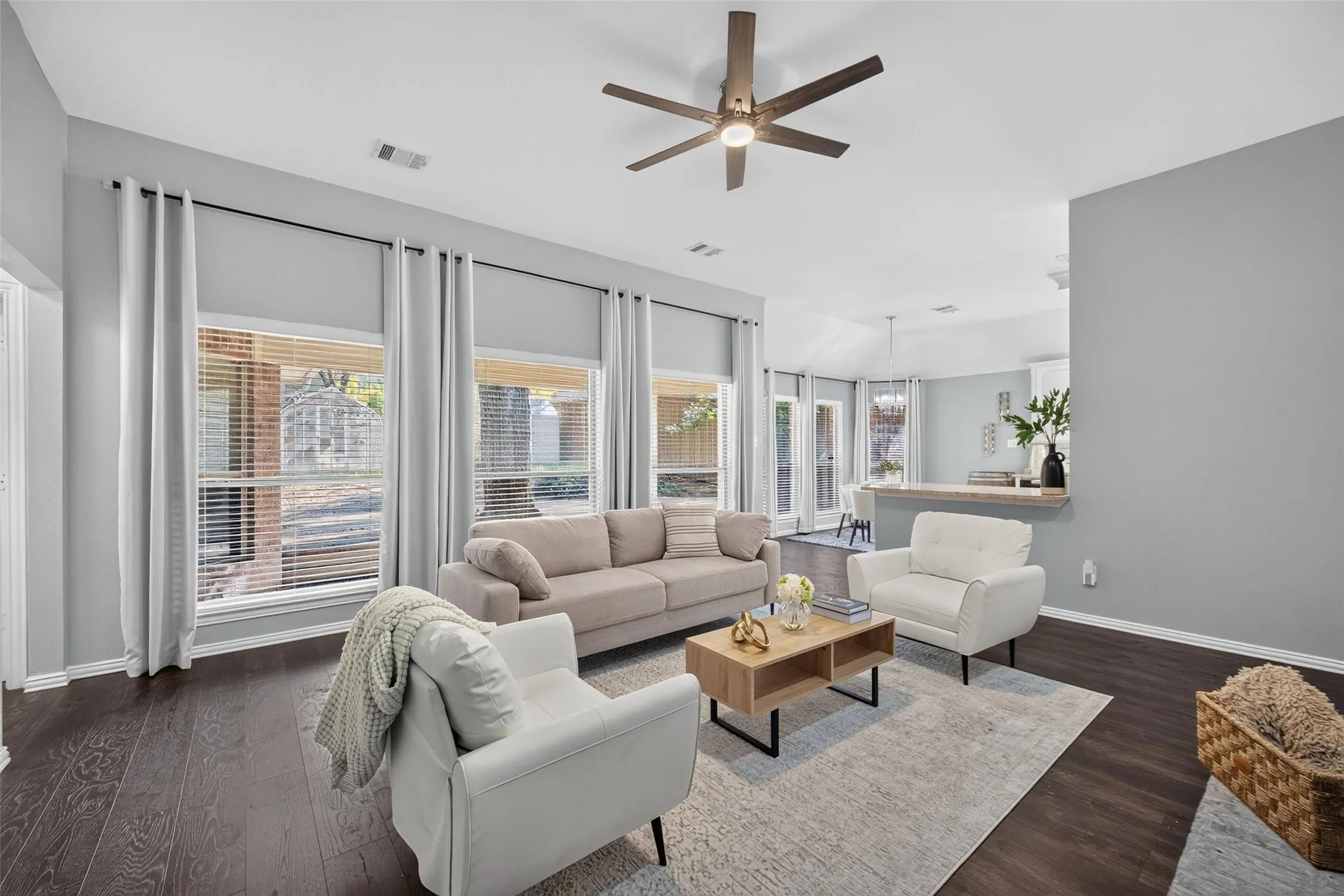 Spacious living area featuring wood-finish flooring, a ceiling fan, and multiple windows