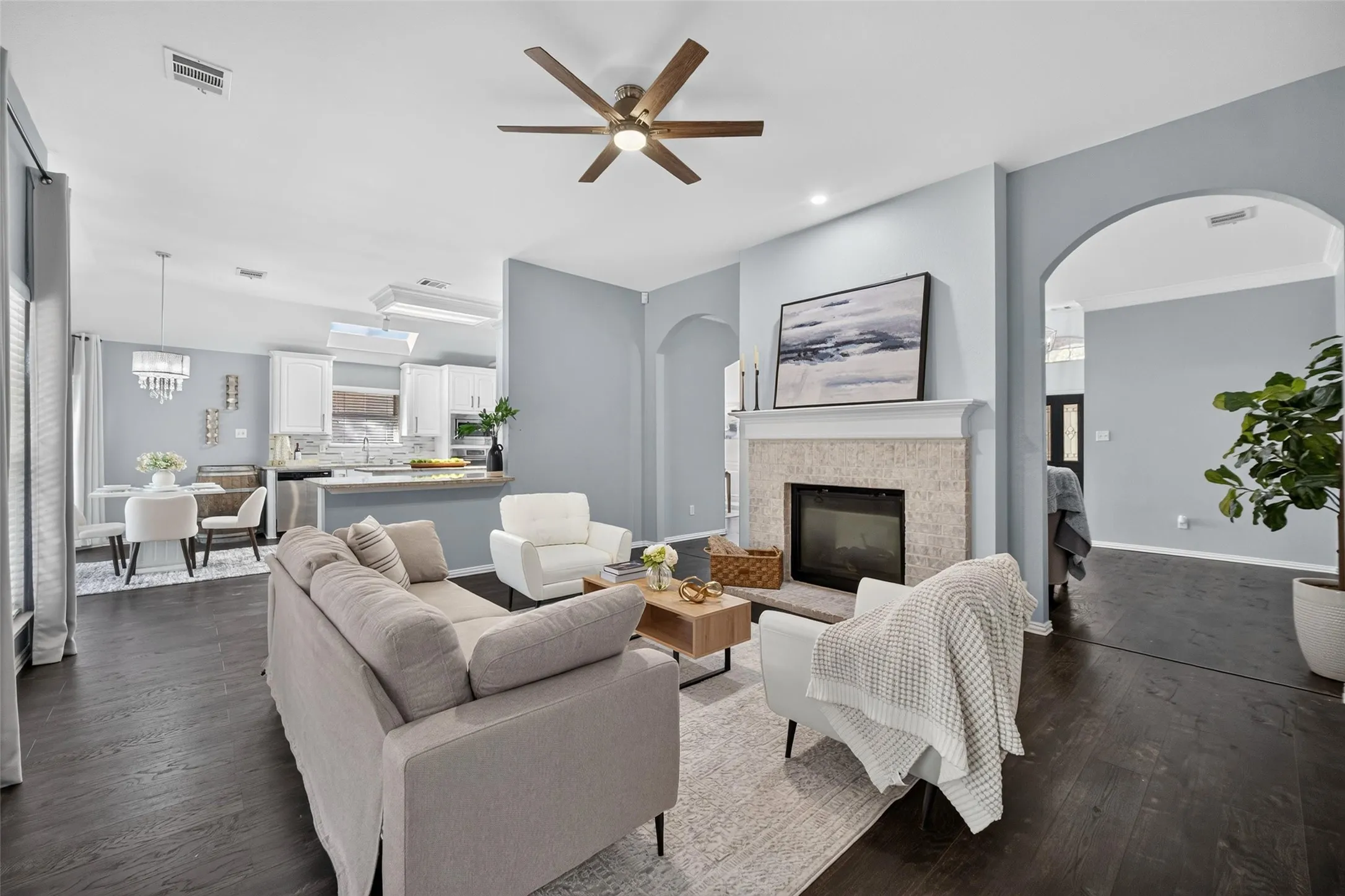 Living area featuring dark wood-finish flooring, a ceiling fan, and a fireplace with a stone surround
