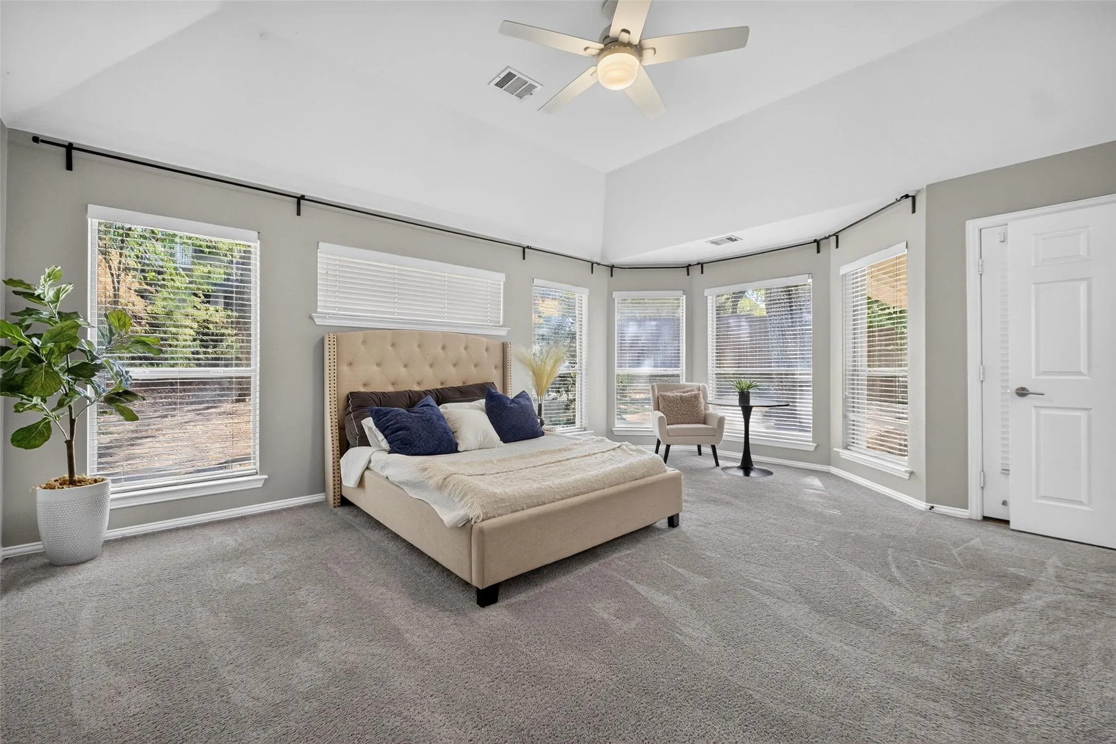 Vaulted ceiling, multiple windows with blinds, gray carpet flooring, ceiling fan with light fixture, and white interior door