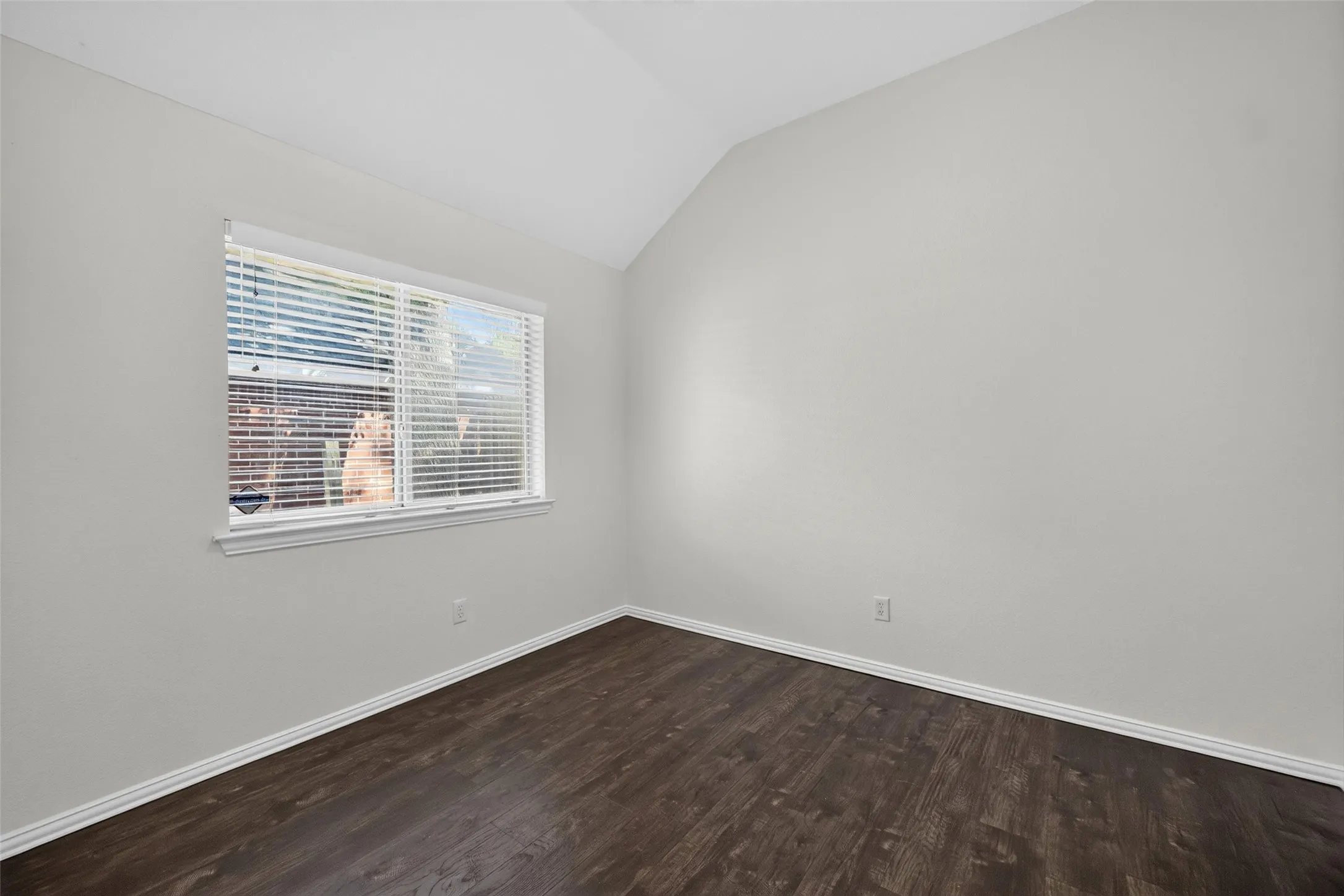 Vaulted ceiling, white walls, wood-finish flooring, white window trim, and white baseboards