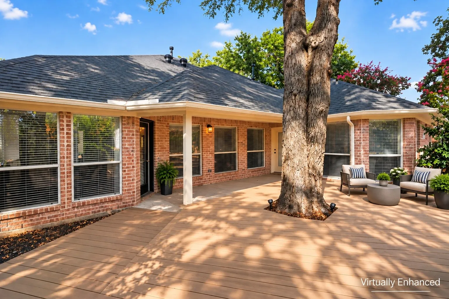 Expansive composite deck, red brick exterior, multiple large windows, covered patio area, and mature trees