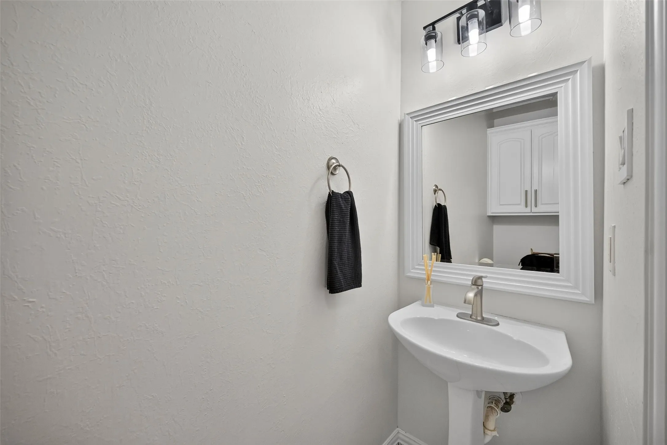 Pedestal sink with a single-handle faucet, framed mirror, and a three-light vanity fixture