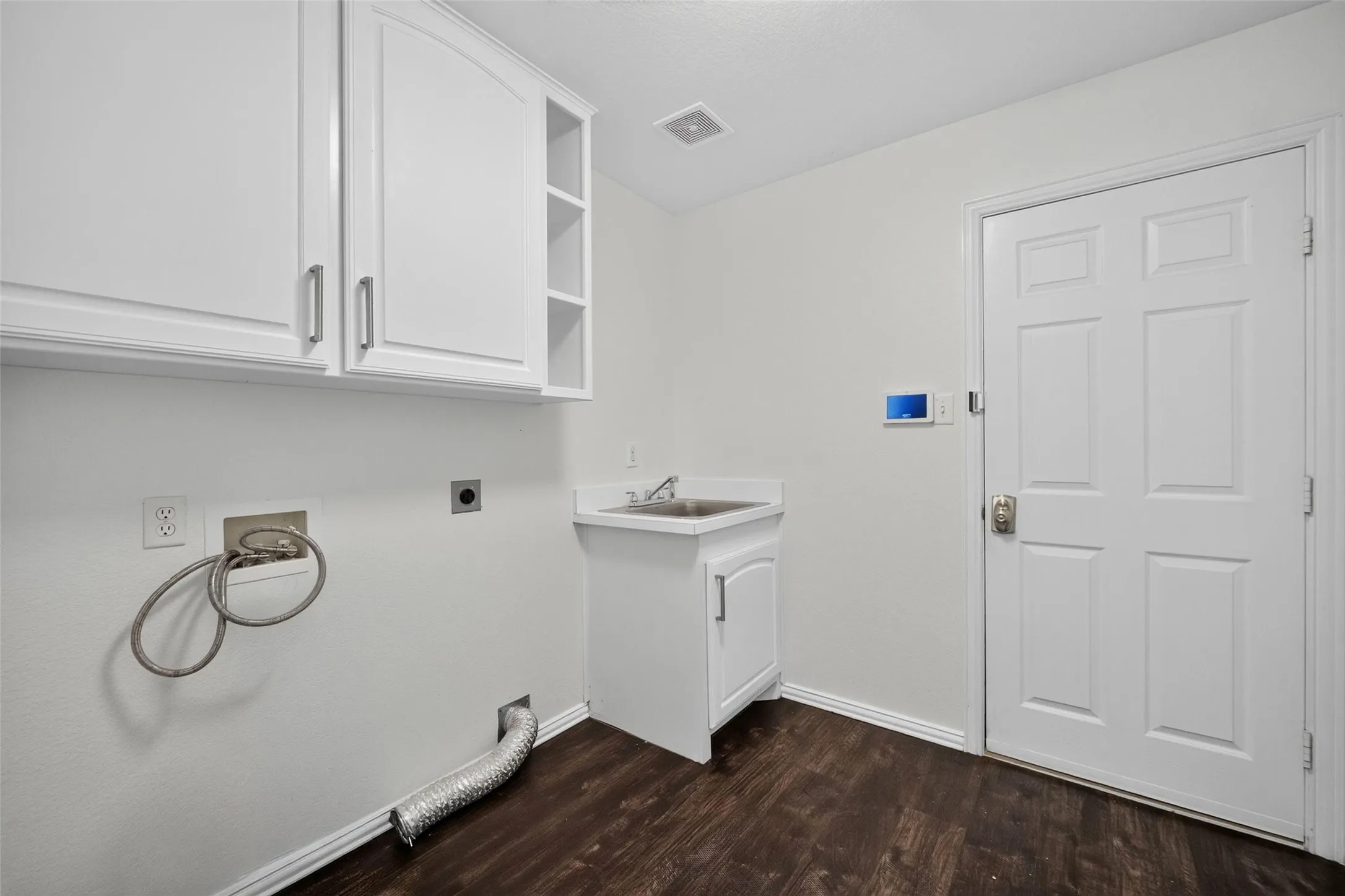 White cabinetry with brushed nickel hardware, utility sink, dark wood-finish flooring, and white paneled door