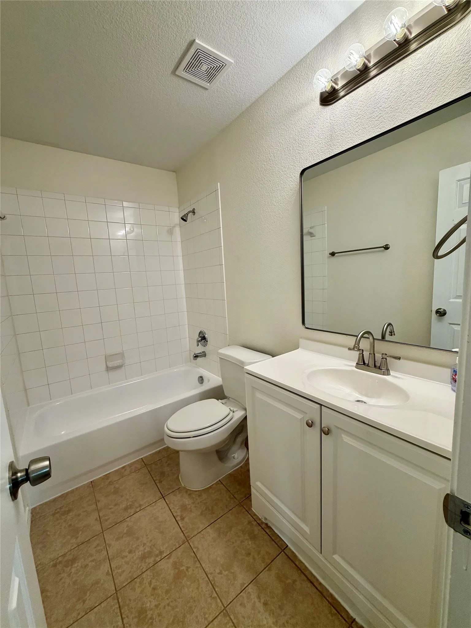 Full bathroom featuring a white vanity with integrated sink, brushed nickel fixtures, a tub/shower combination with white subway tile surround, and neutral tile flooring