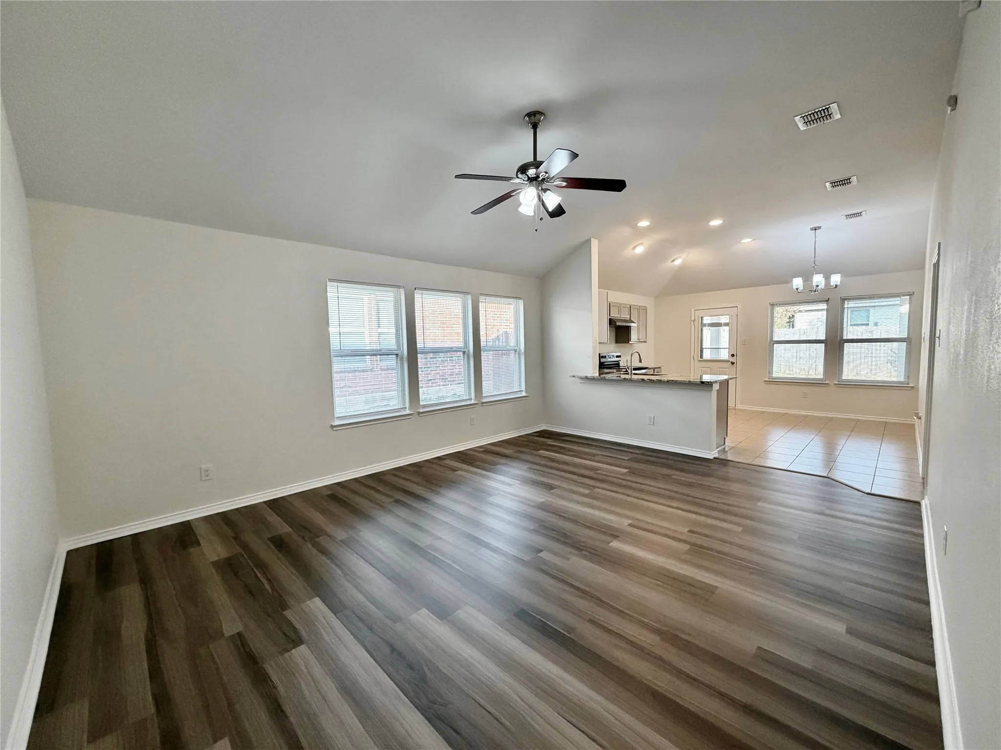 Spacious living area with wood-finish flooring, ample natural light from multiple windows, and a ceiling fan