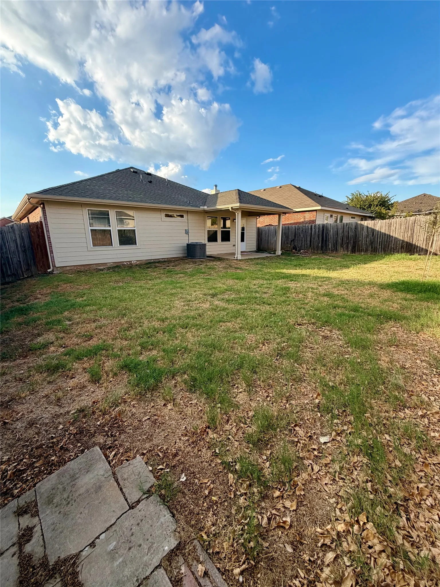 Expansive backyard with a covered patio, tan siding, and a gabled roof