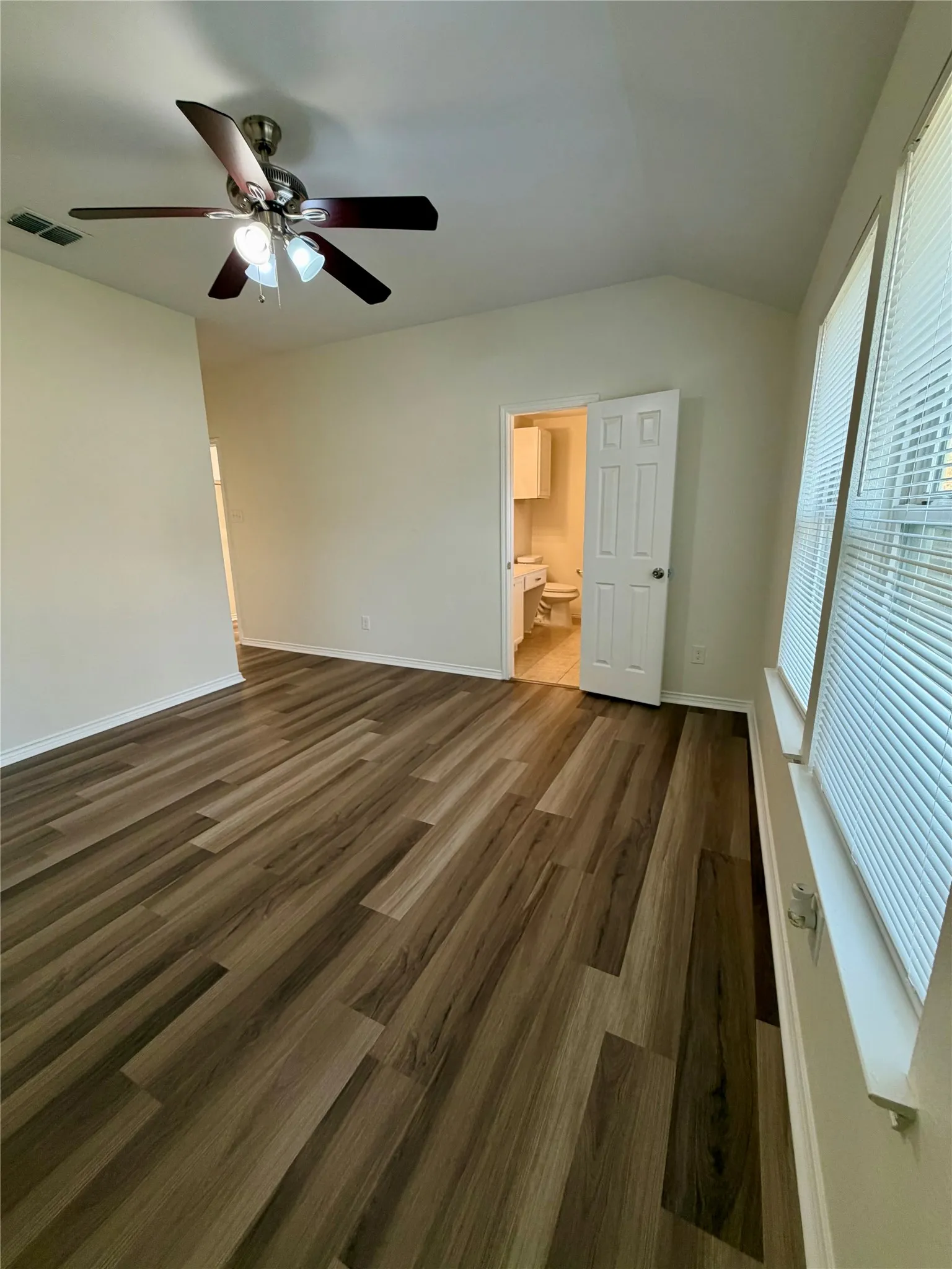 Vaulted ceiling with a ceiling fan, wood-finish flooring, and multiple windows with blinds