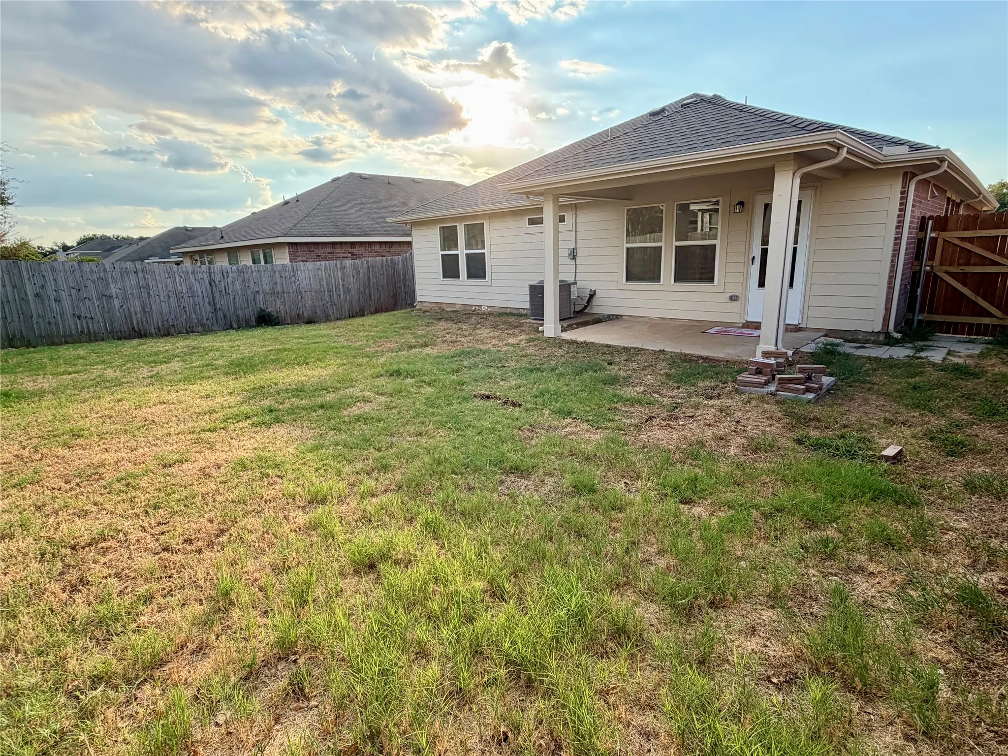 Expansive backyard with a full privacy fence, covered patio, and brick exterior accents