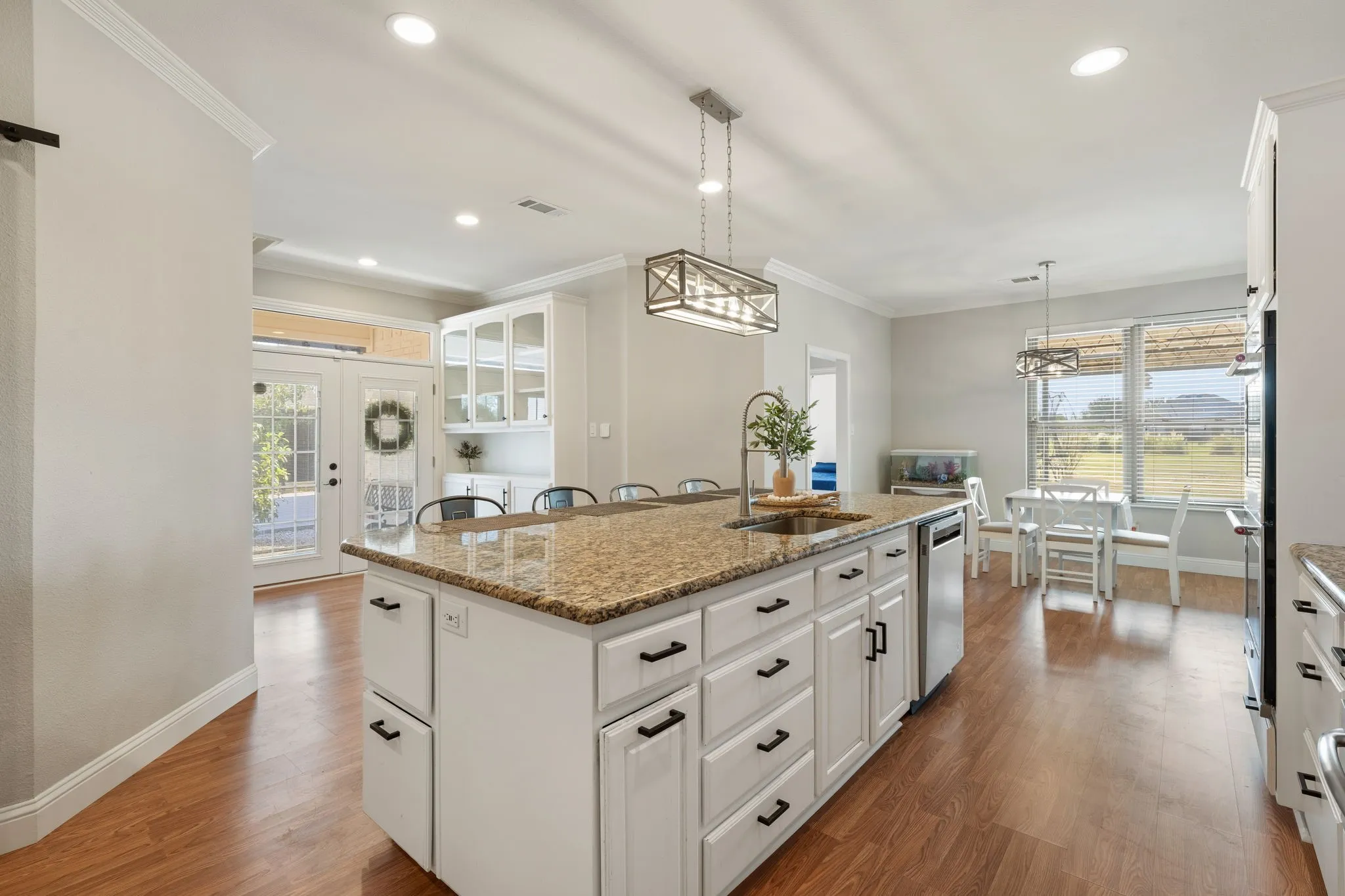 Kitchen featuring a large island with an undermount sink, ample cabinetry, wood-finish flooring, recessed lighting, and a built-in dishwasher