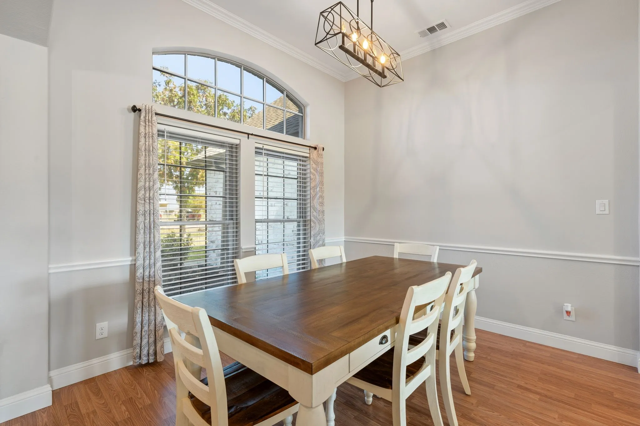 Arch-top window with multiple panes, wood-finish flooring, crown molding, and wainscoting