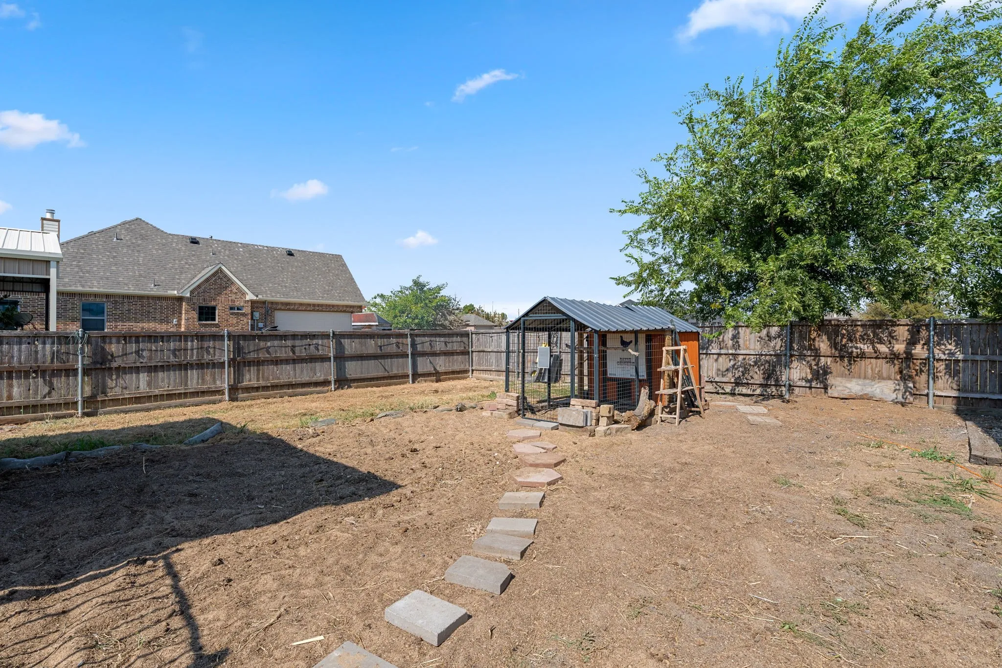 Fenced backyard featuring a chicken coop structure, a stone paver path, and a partially cultivated garden area
