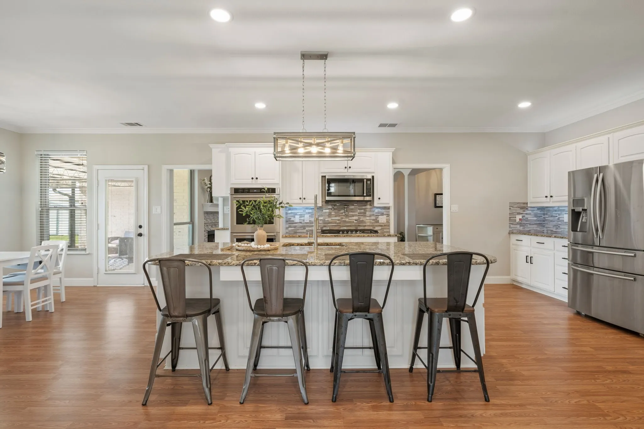 Open-concept kitchen featuring an oversized island with seating, stainless steel appliances, white cabinetry, and wood-finish flooring