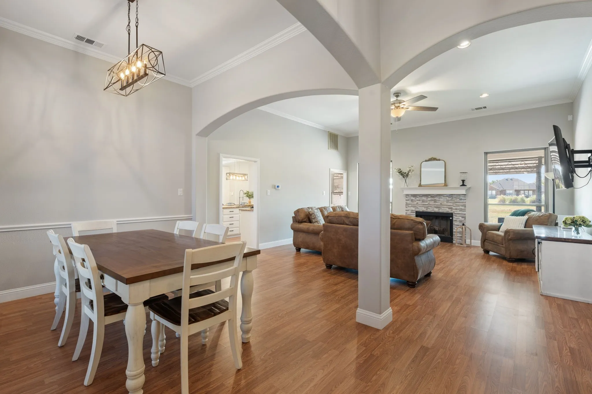 Expansive open living area featuring wood-finish flooring, arched architectural details, crown molding, and a stone-clad fireplace