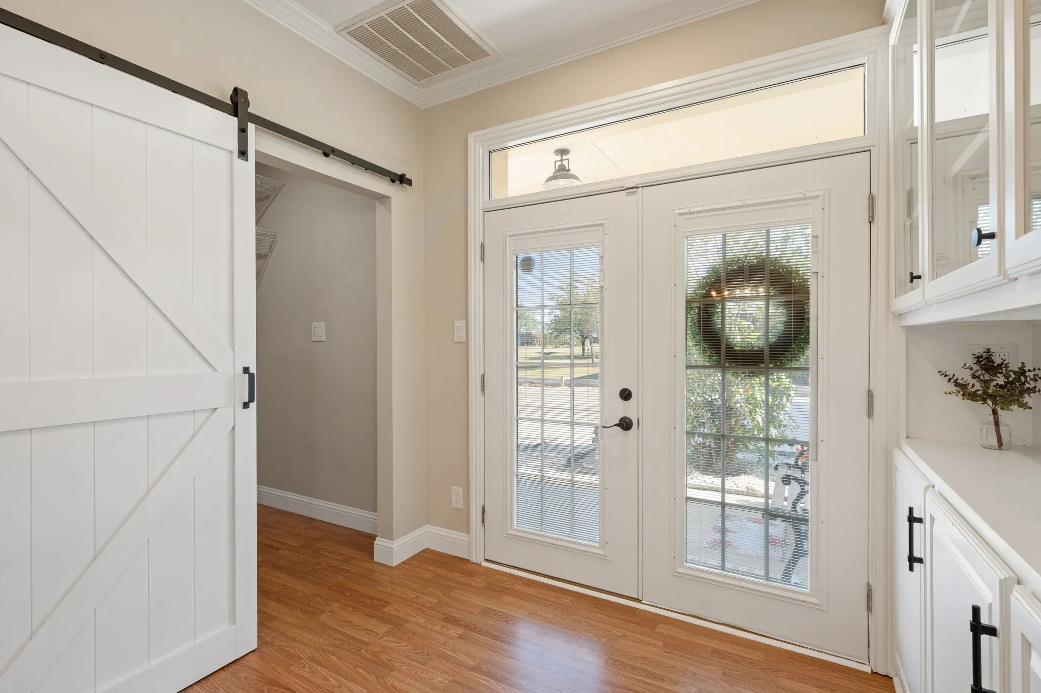 Wood-finish flooring, white barn door, double glass-paneled entry doors with transom, and built-in cabinetry with glass-front uppers
