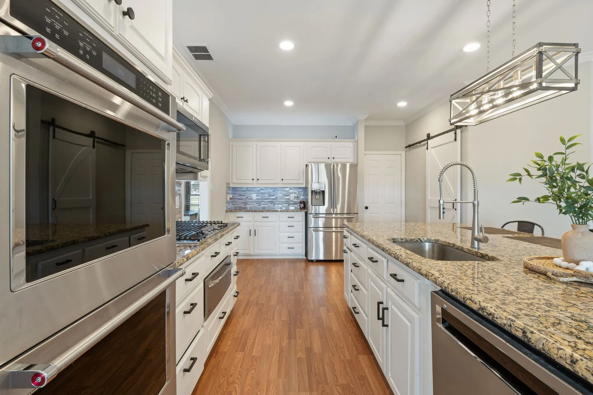 Kitchen featuring light wood-finish flooring, white cabinetry with dark hardware, stainless steel appliances, and granite countertops