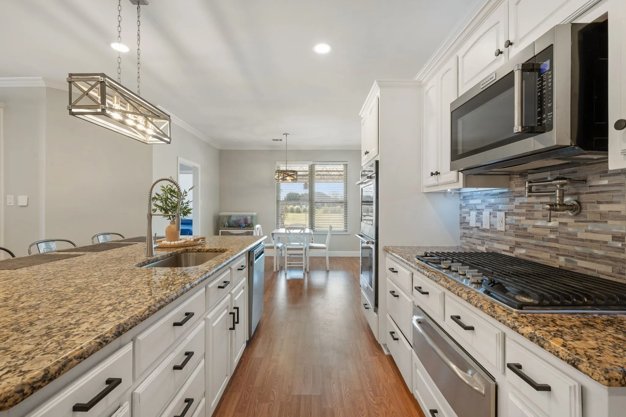 Gourmet kitchen featuring granite countertops, stainless steel appliances, a tiled backsplash, wood-finish flooring, and white cabinetry with dark hardware