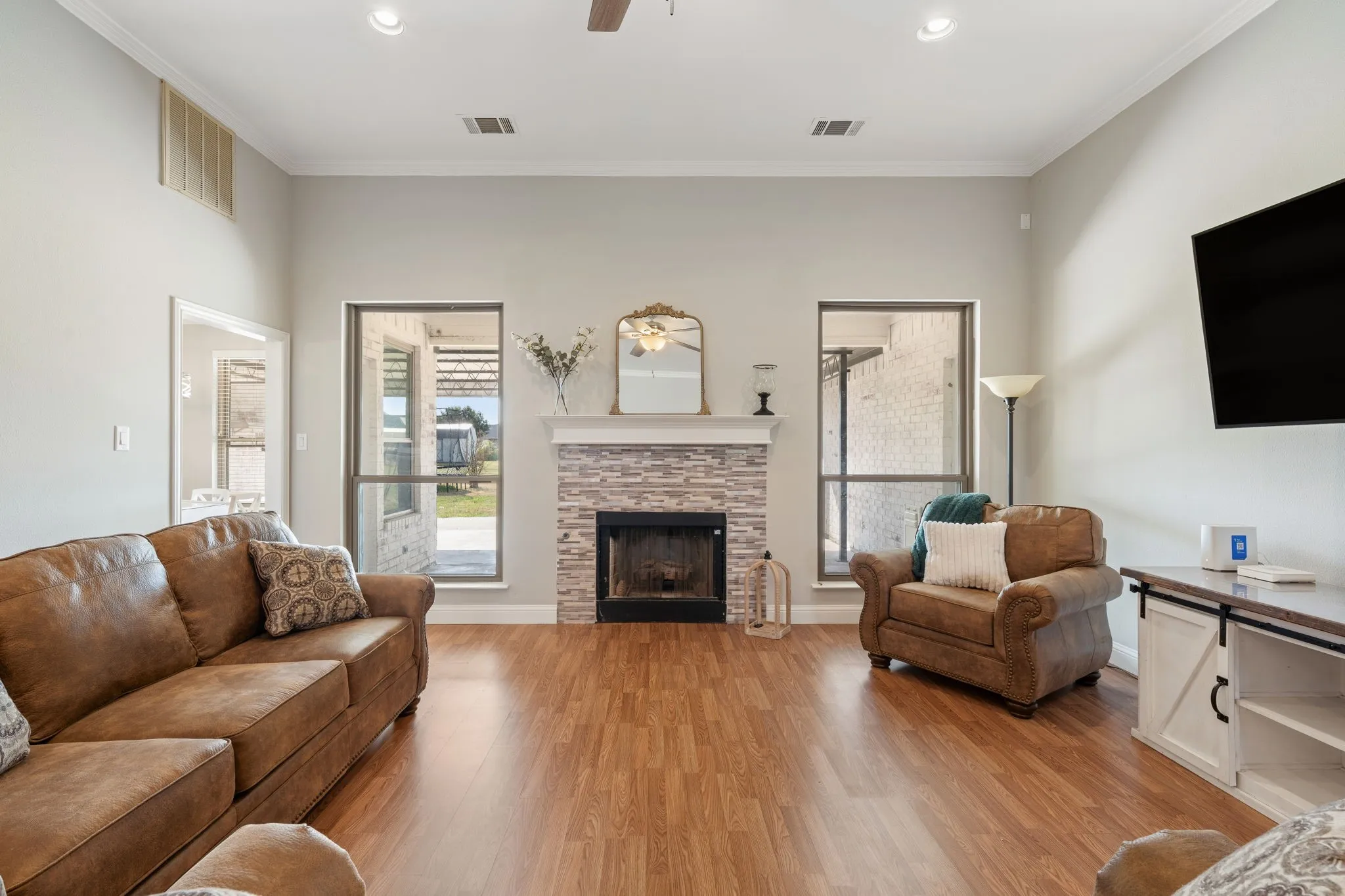 High ceilings with crown molding, wood-finish flooring, a stacked stone fireplace, large windows, and recessed lighting