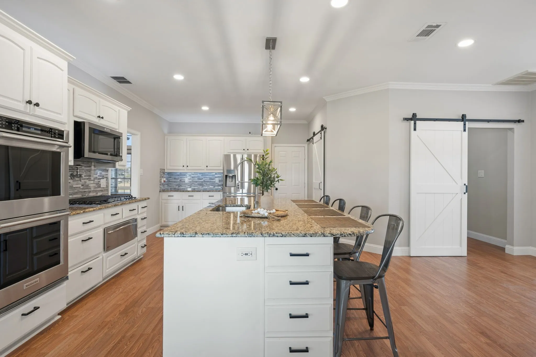 Kitchen featuring a large island with stone countertop, stainless steel appliances, white cabinetry, and wood-finish flooring