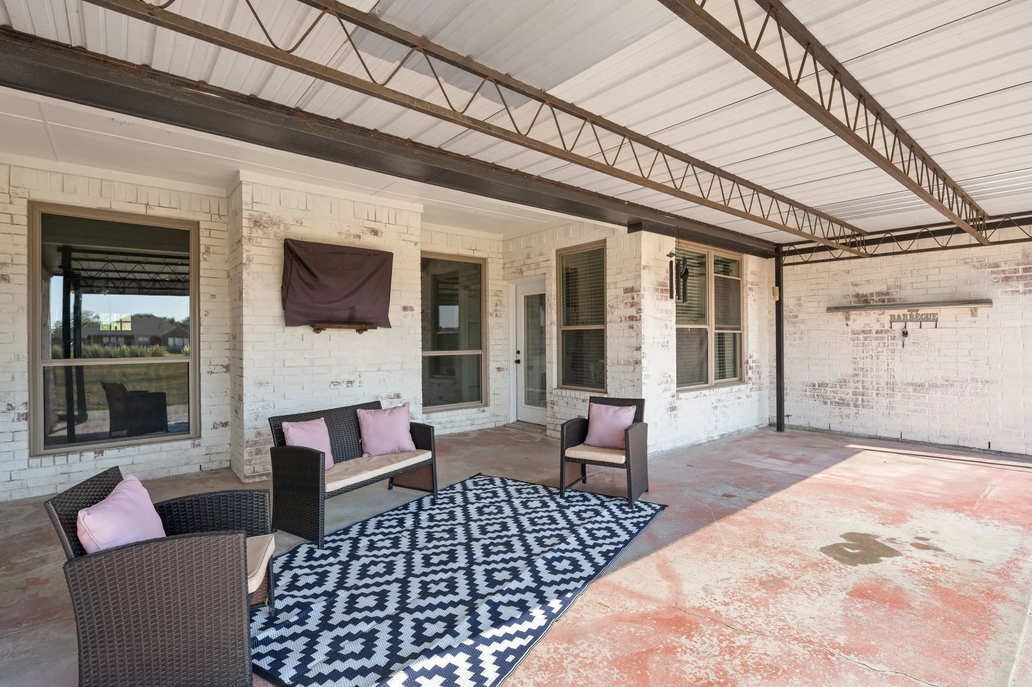 Covered patio featuring a metal roof structure, brick exterior, and multiple window openings