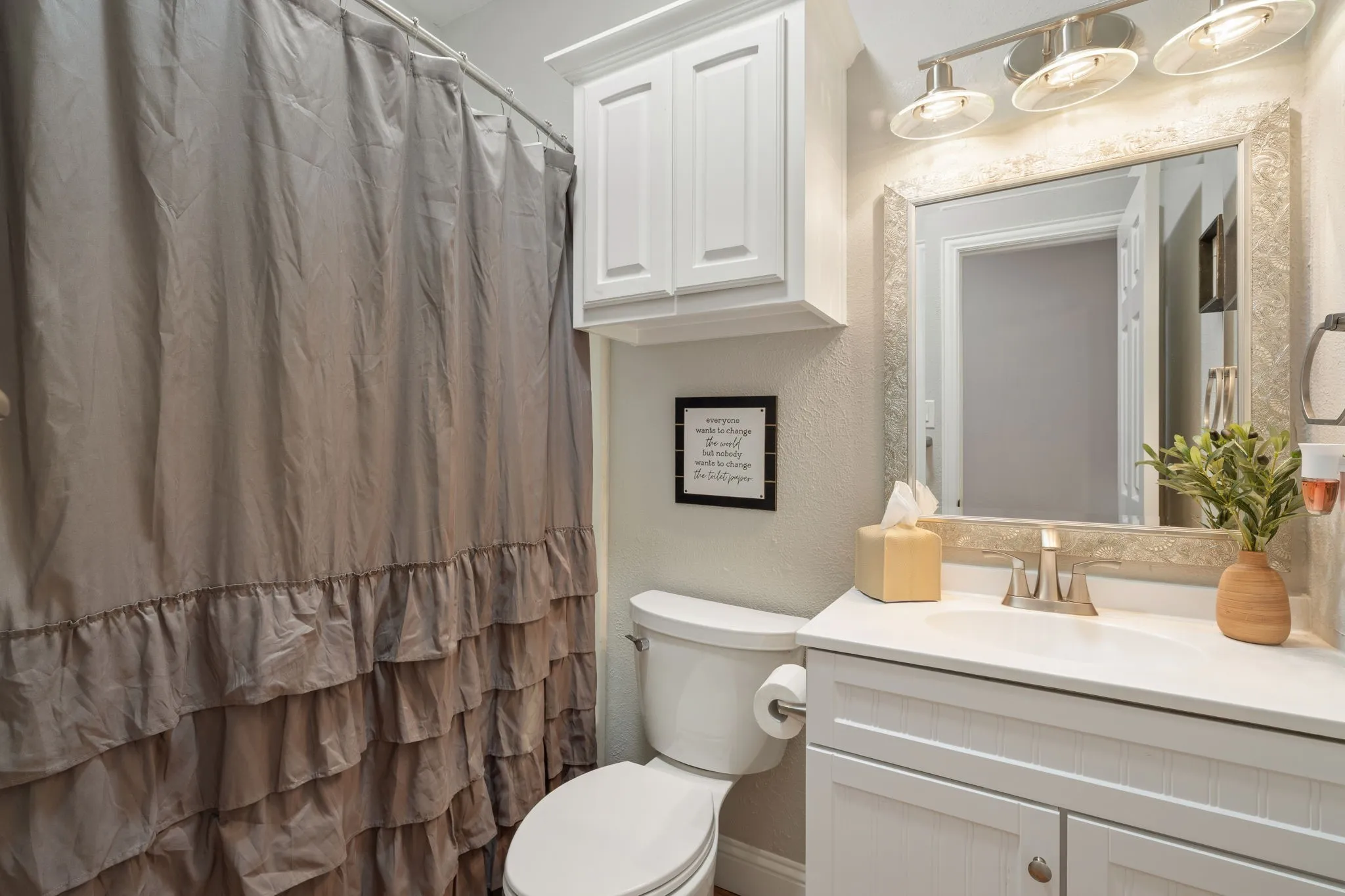 White vanity with brushed nickel hardware, single basin sink, and a mounted mirror with decorative frame
