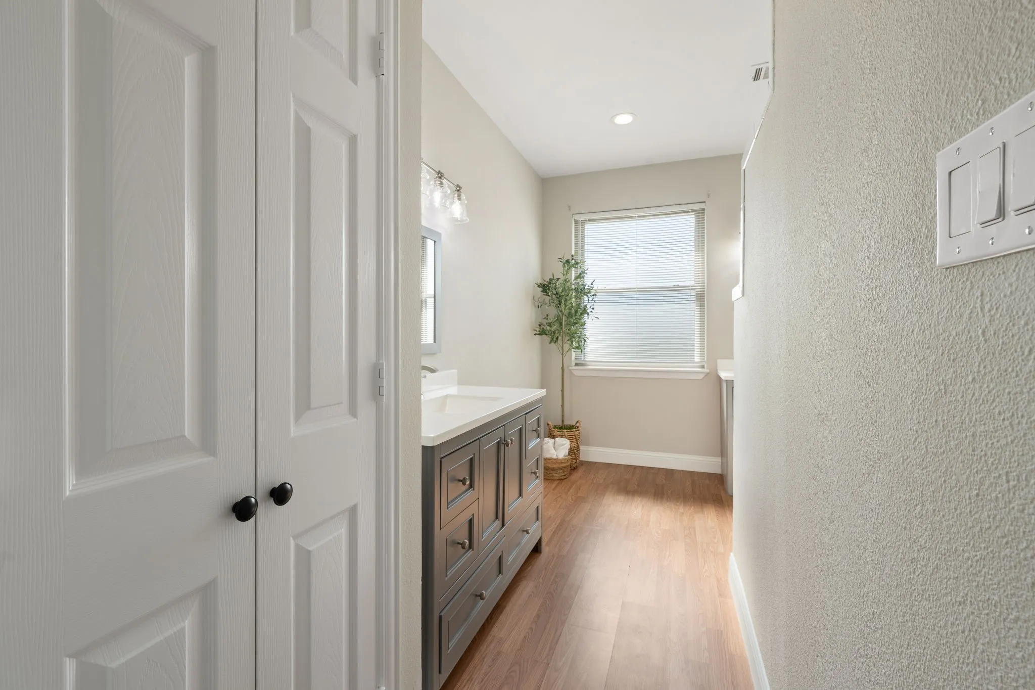 Wood-finish flooring, single window, recessed lighting, vanity with built-in storage, and wall-mounted light fixture