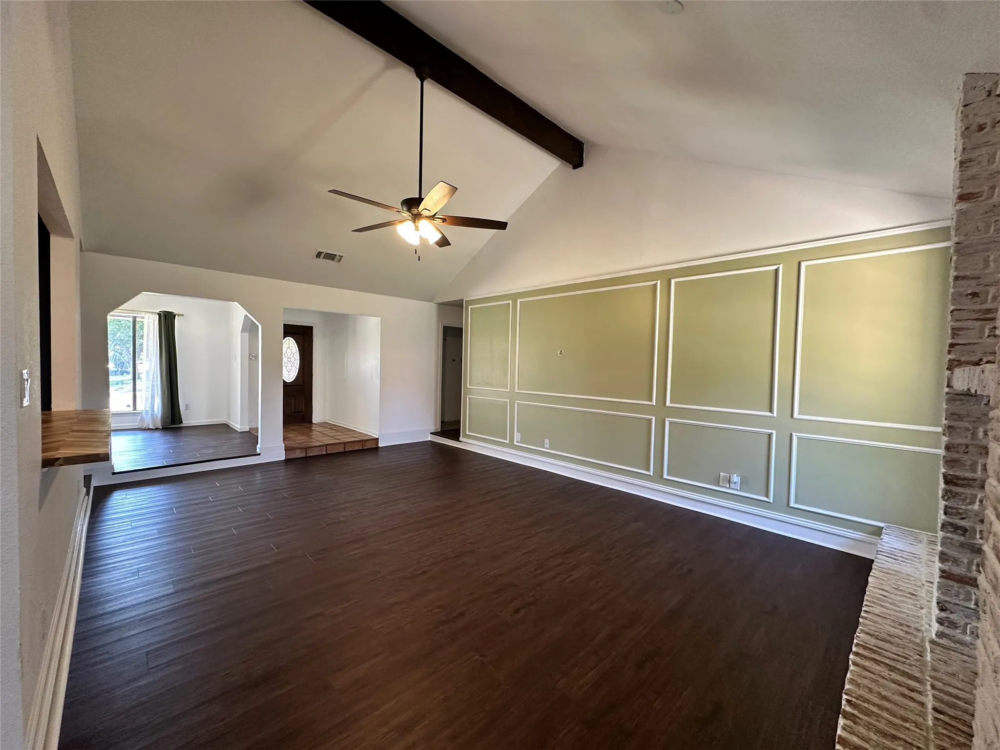 Vaulted ceiling with exposed wood beam, wood-finish flooring, accent wall with decorative molding, and brick column