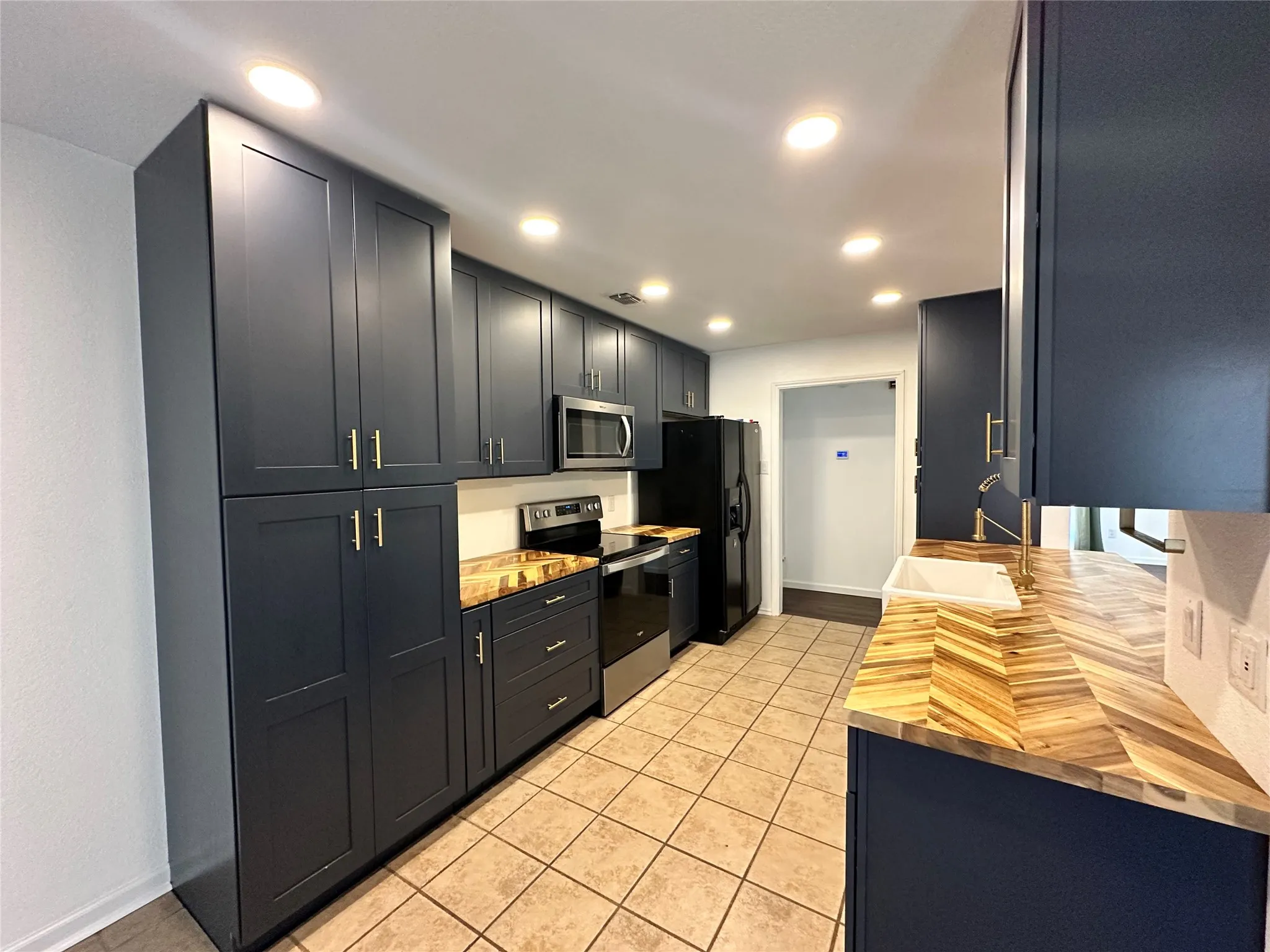 Kitchen featuring dark blue cabinetry, wood-finish countertops, stainless steel appliances, ceramic tile flooring, and recessed lighting