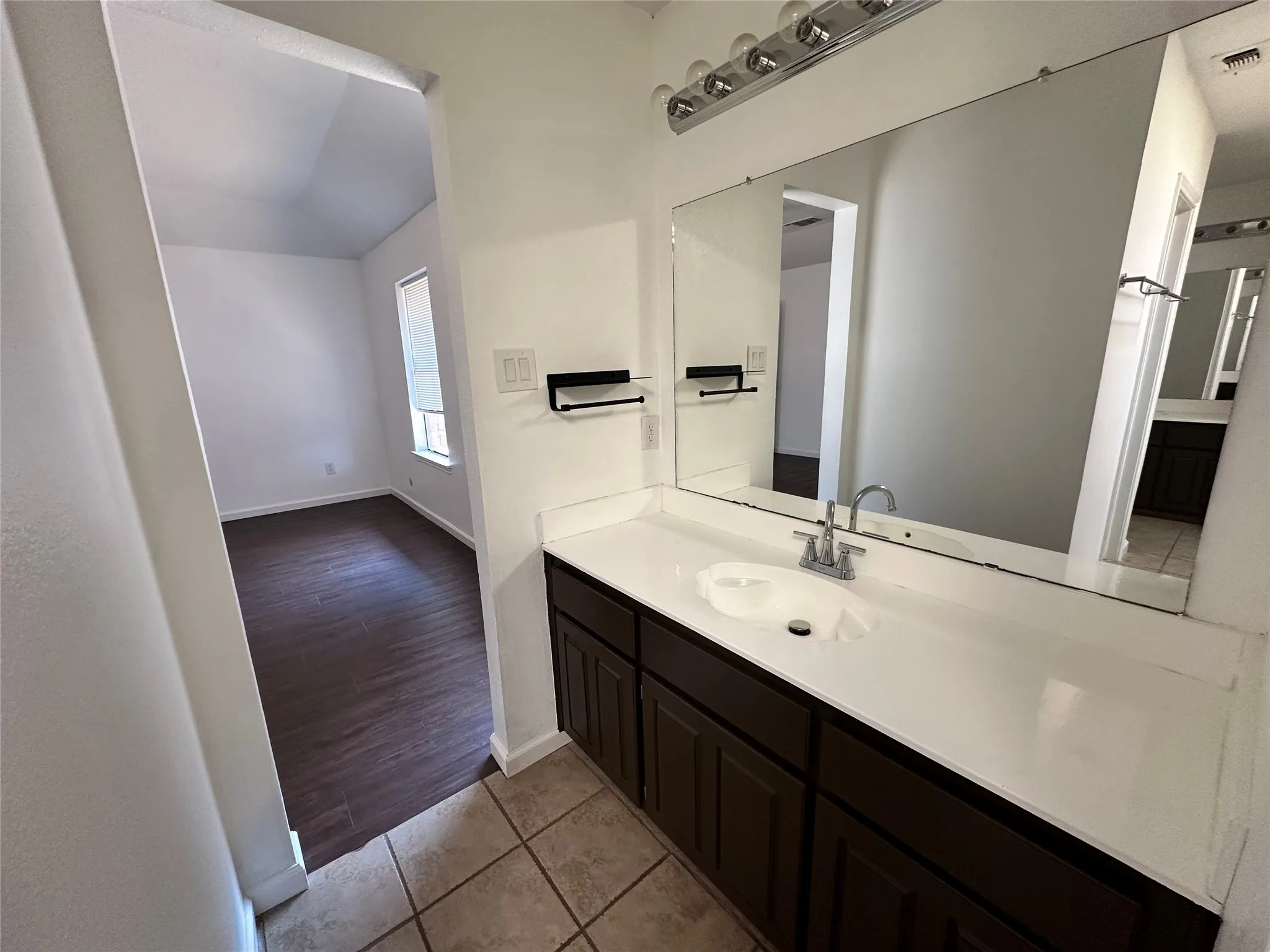 White vanity with integrated sink, chrome faucet, and expansive mirror with overhead lighting