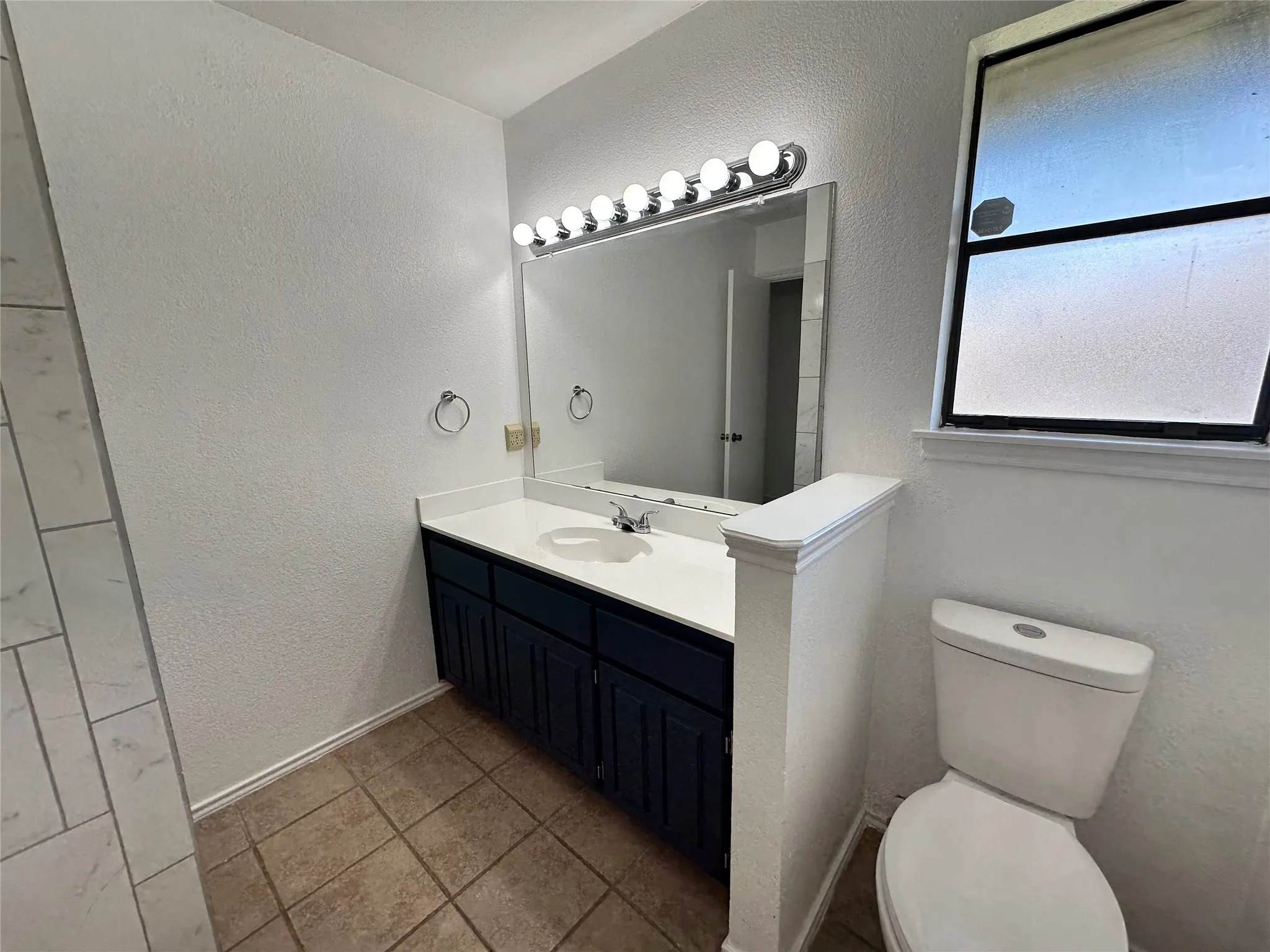Vanity with a white countertop and integrated sink, dark cabinetry, and tile flooring