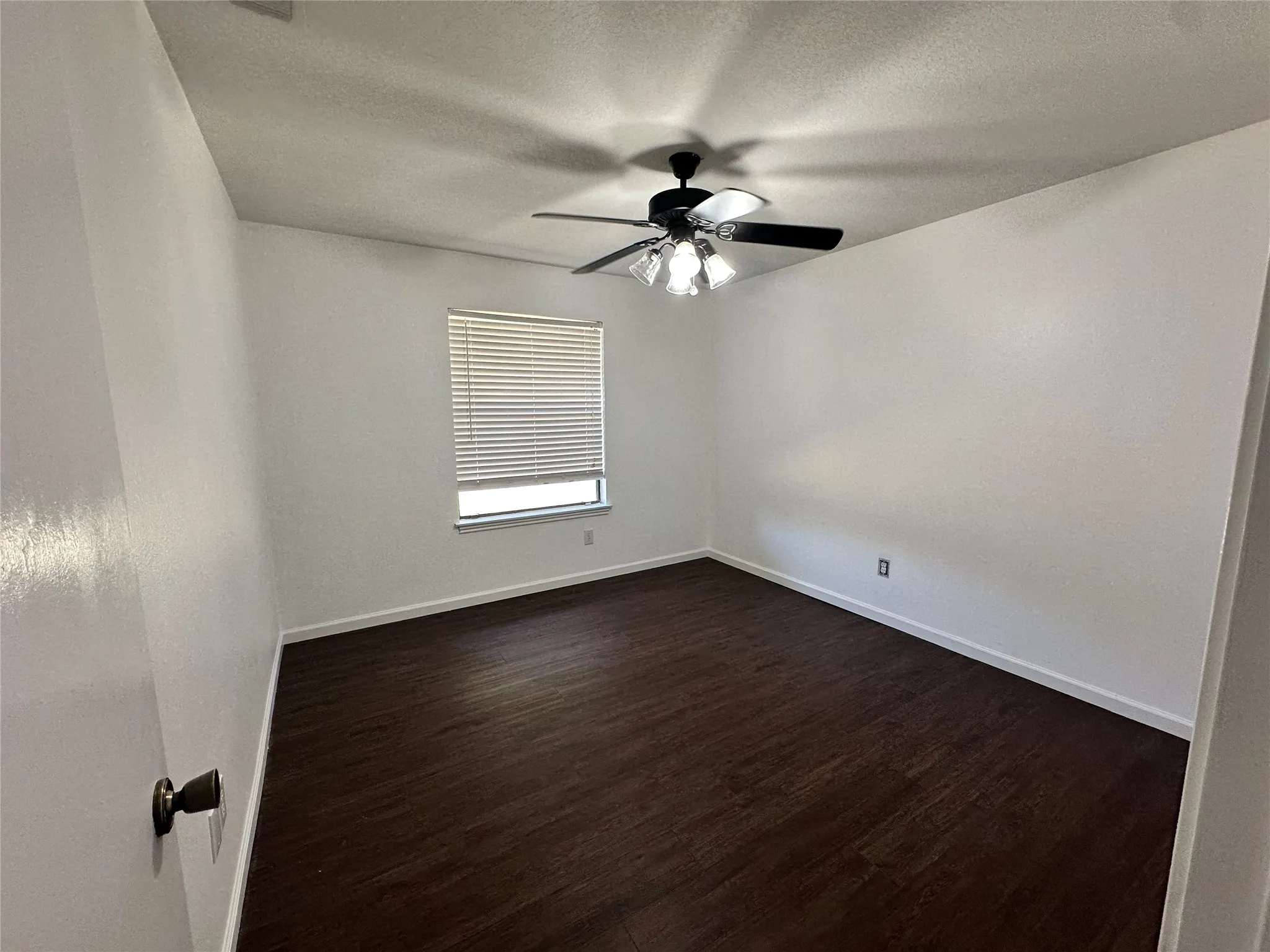 Wood-finish flooring with white baseboards, a ceiling fan with integrated lighting, and a window with horizontal blinds